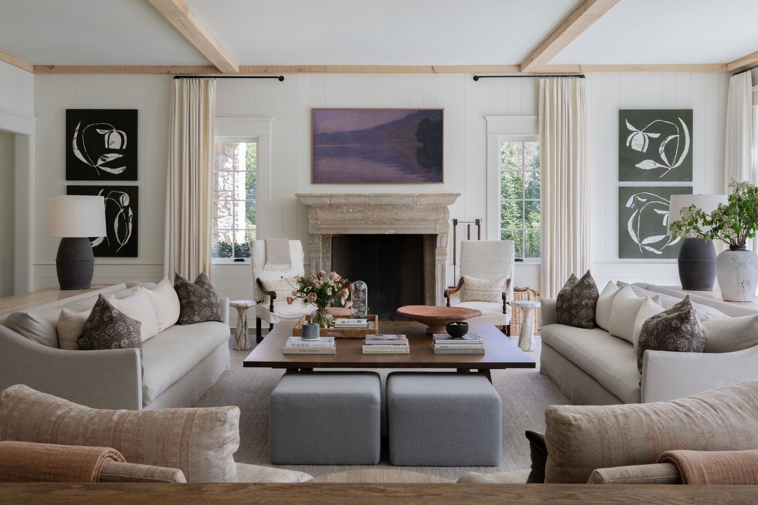 Sophisticated living room with twin sofas, fireplace, abstract art, and neutral tones with blue ottoman accents.