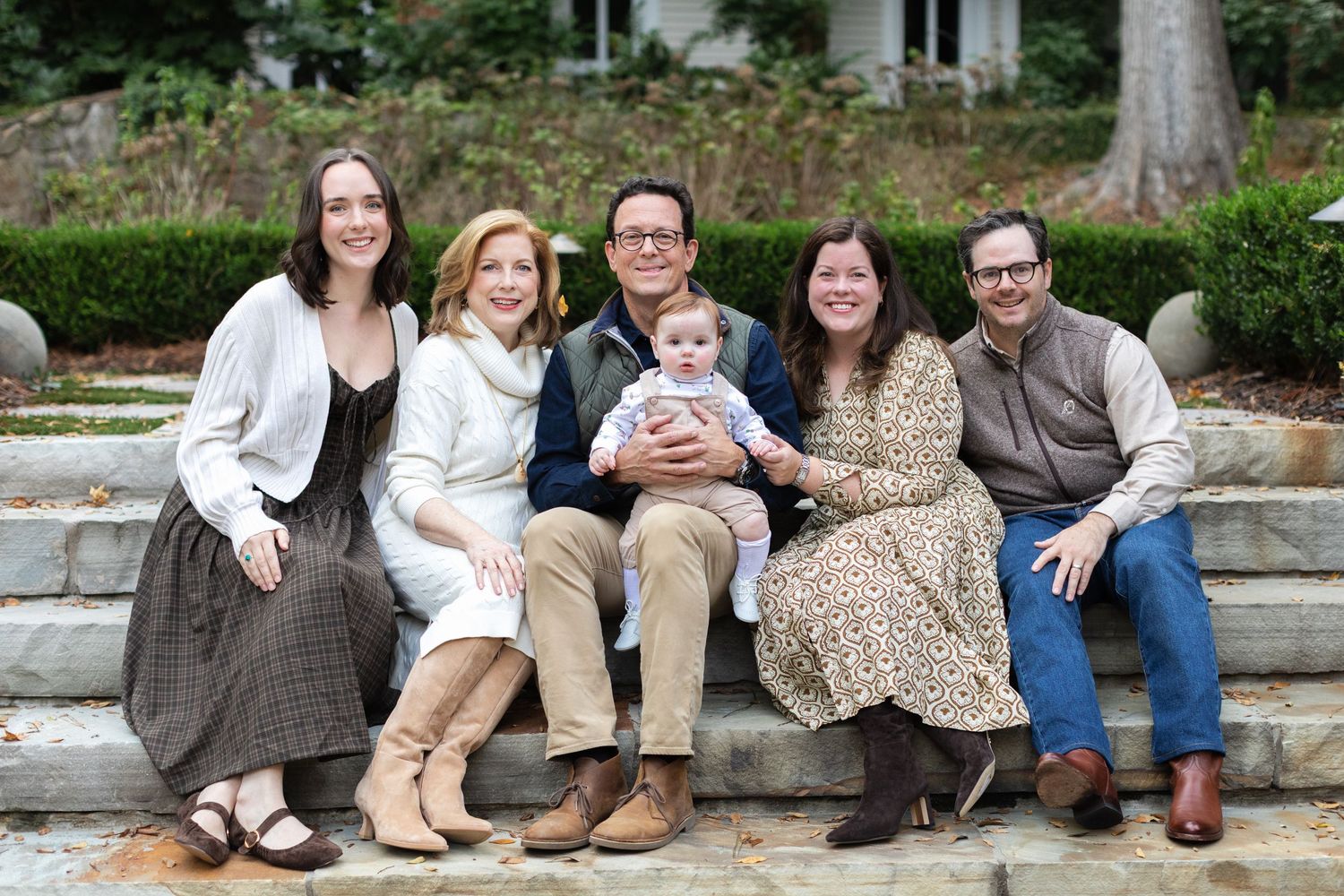 A group of people sitting together on stone steps in a garden setting on a sunny day.