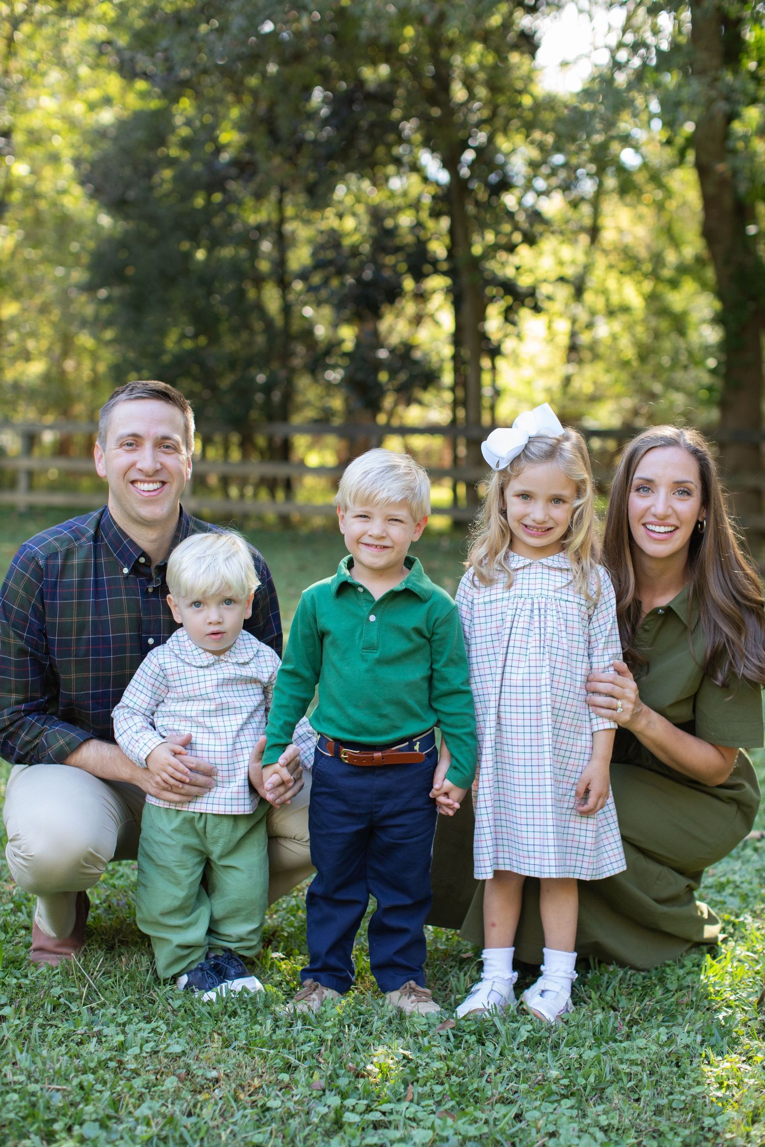 A family of five poses together outdoors on a sunny day wearing coordinated casual clothing.