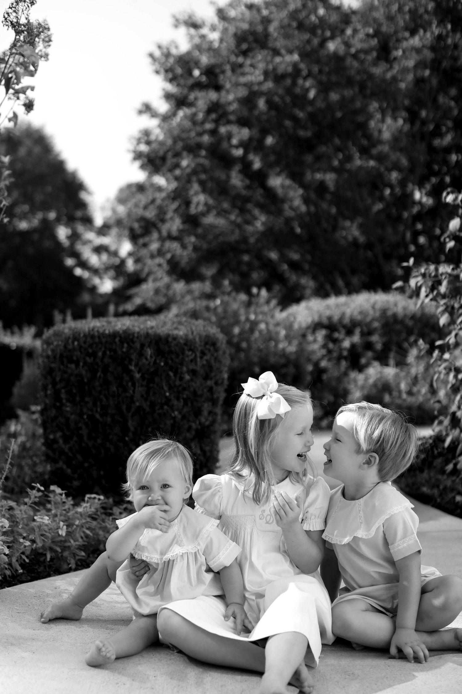 Black and white photo showing playful family lying outdoors in a relaxed pose wearing white clothing.
