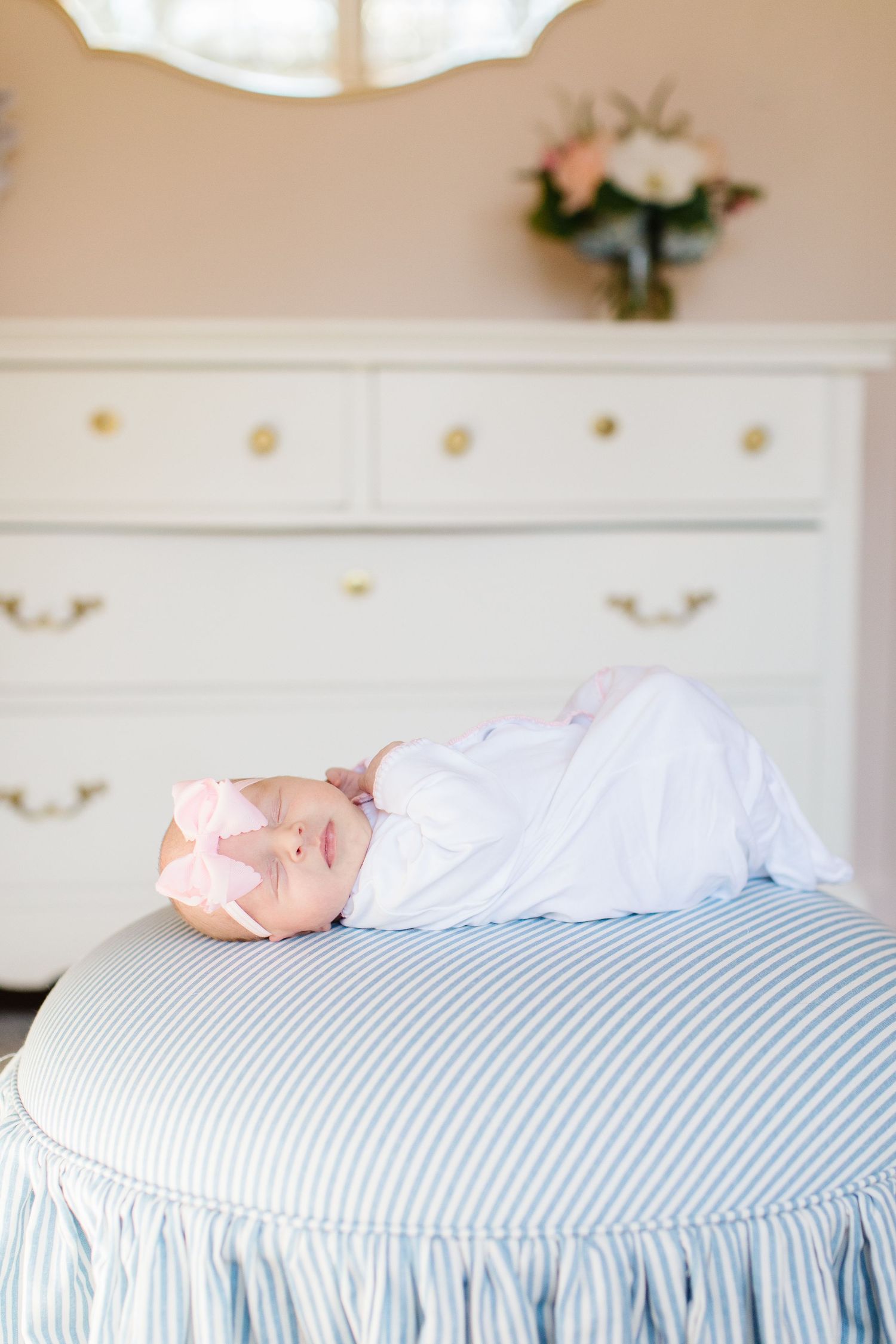 Sleeping baby in pink onesie lying on blue and white striped bedding in a bright nursery setting.