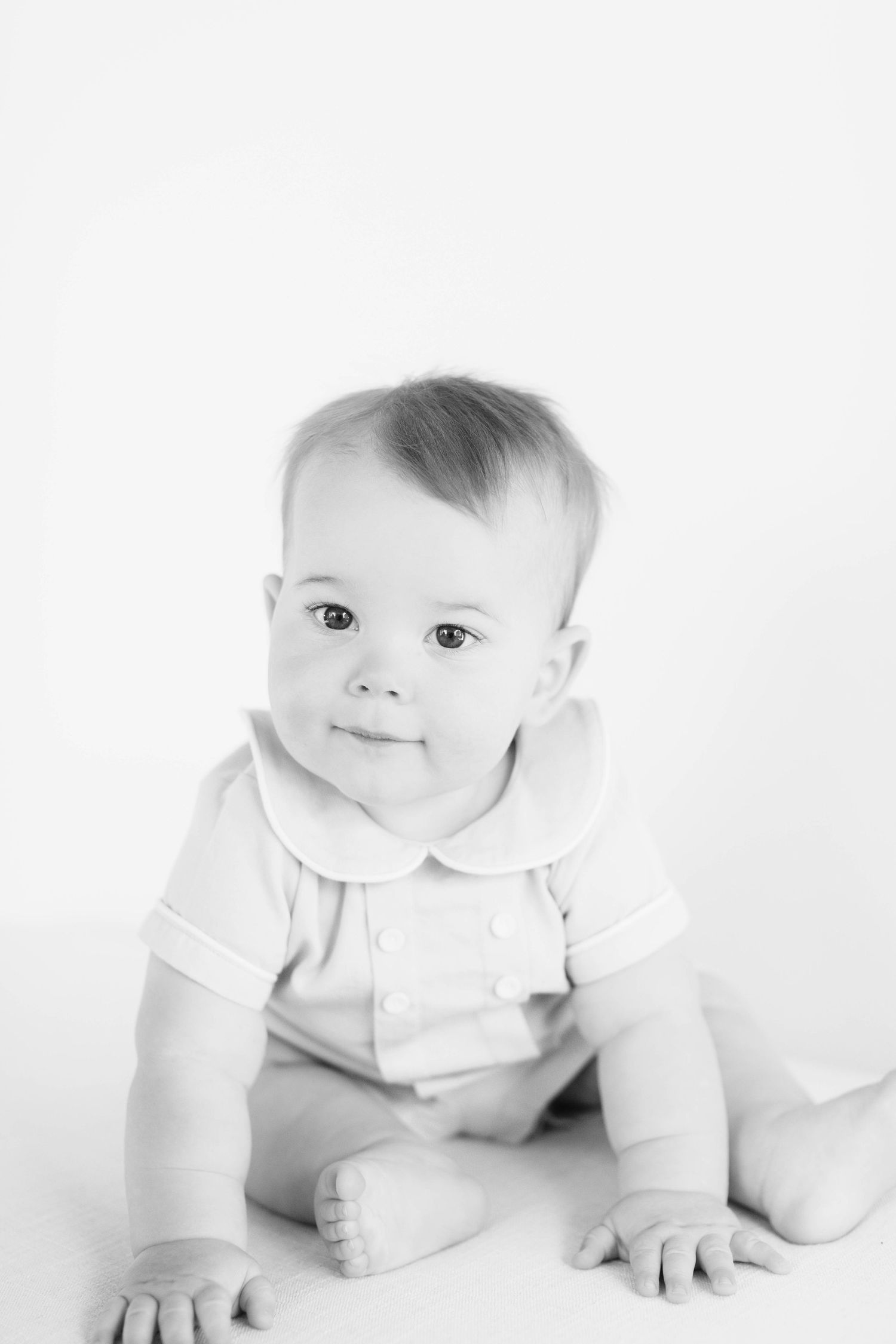 Monochrome studio portrait of baby wearing classic white outfit.