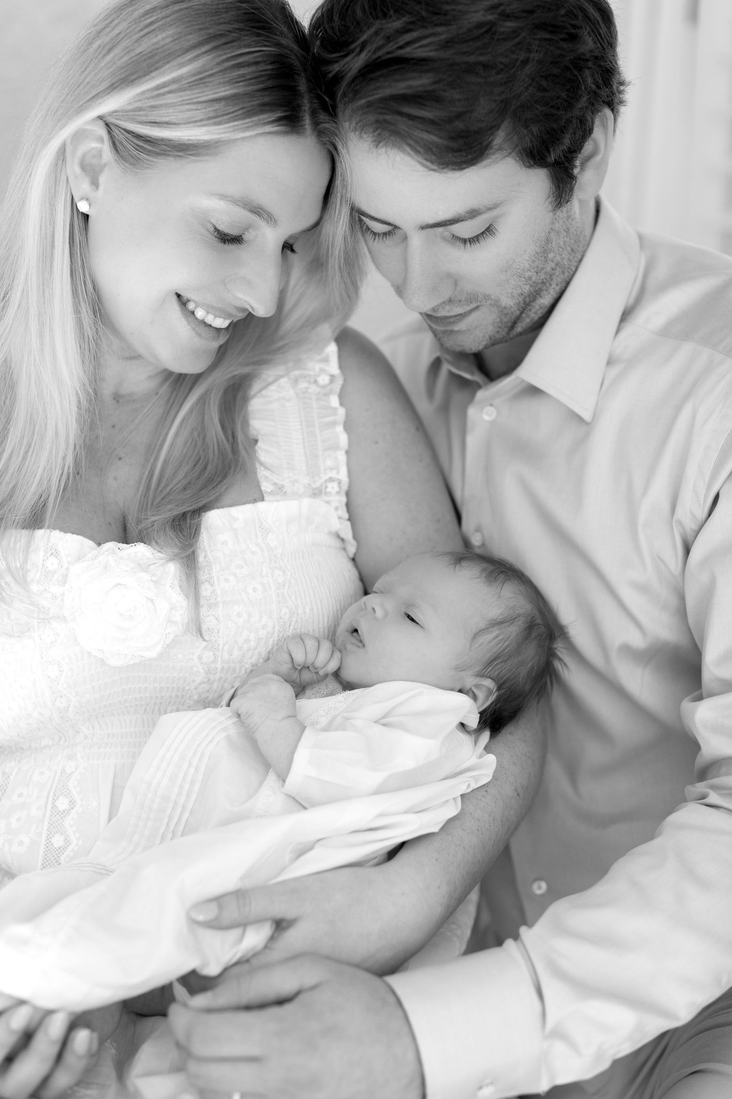 A couple in white clothing shares tender moments with their baby in a series of black and white photographs.