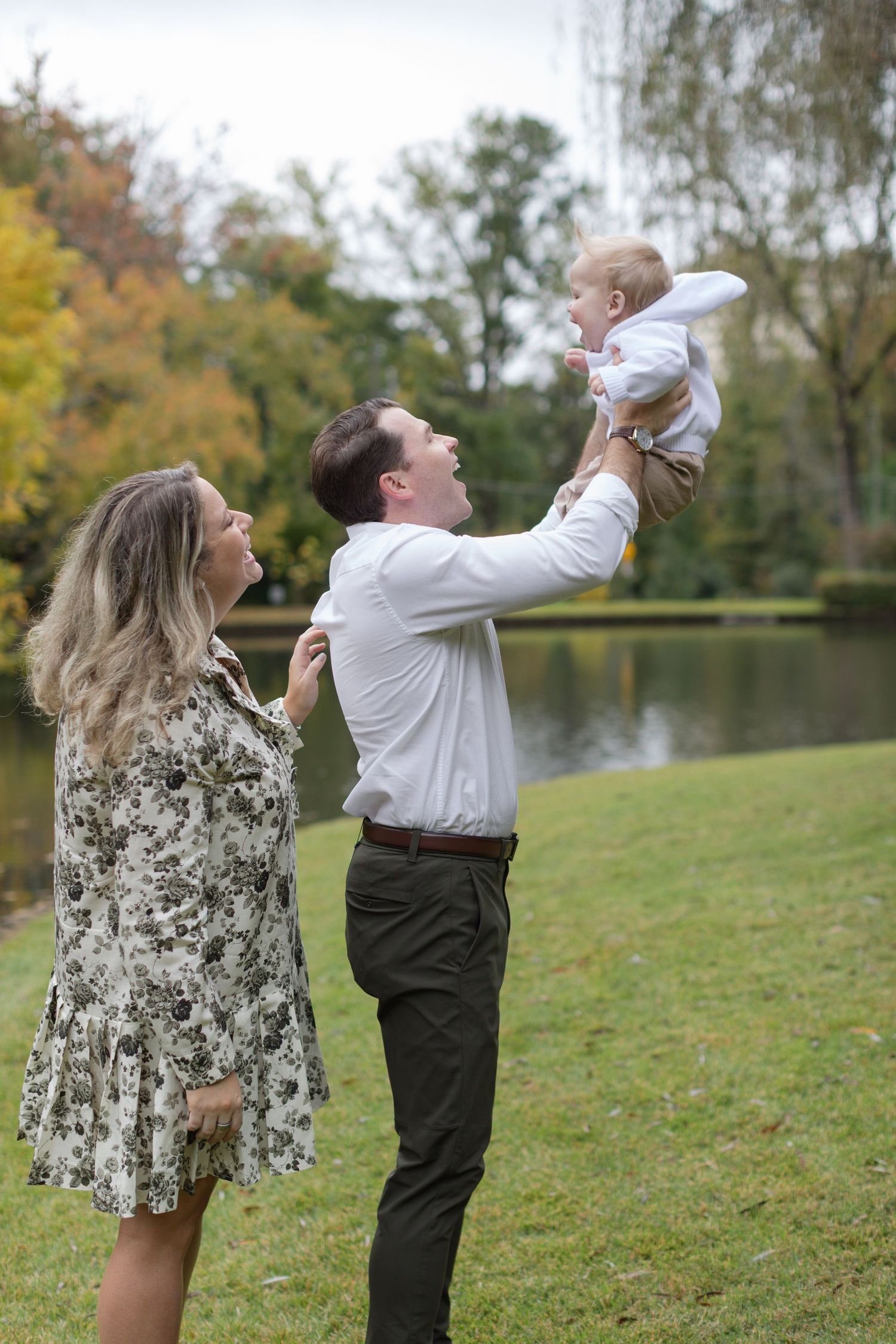 A parent and child play together on a grassy hill near a lake during autumn, shown in a series of candid moments.