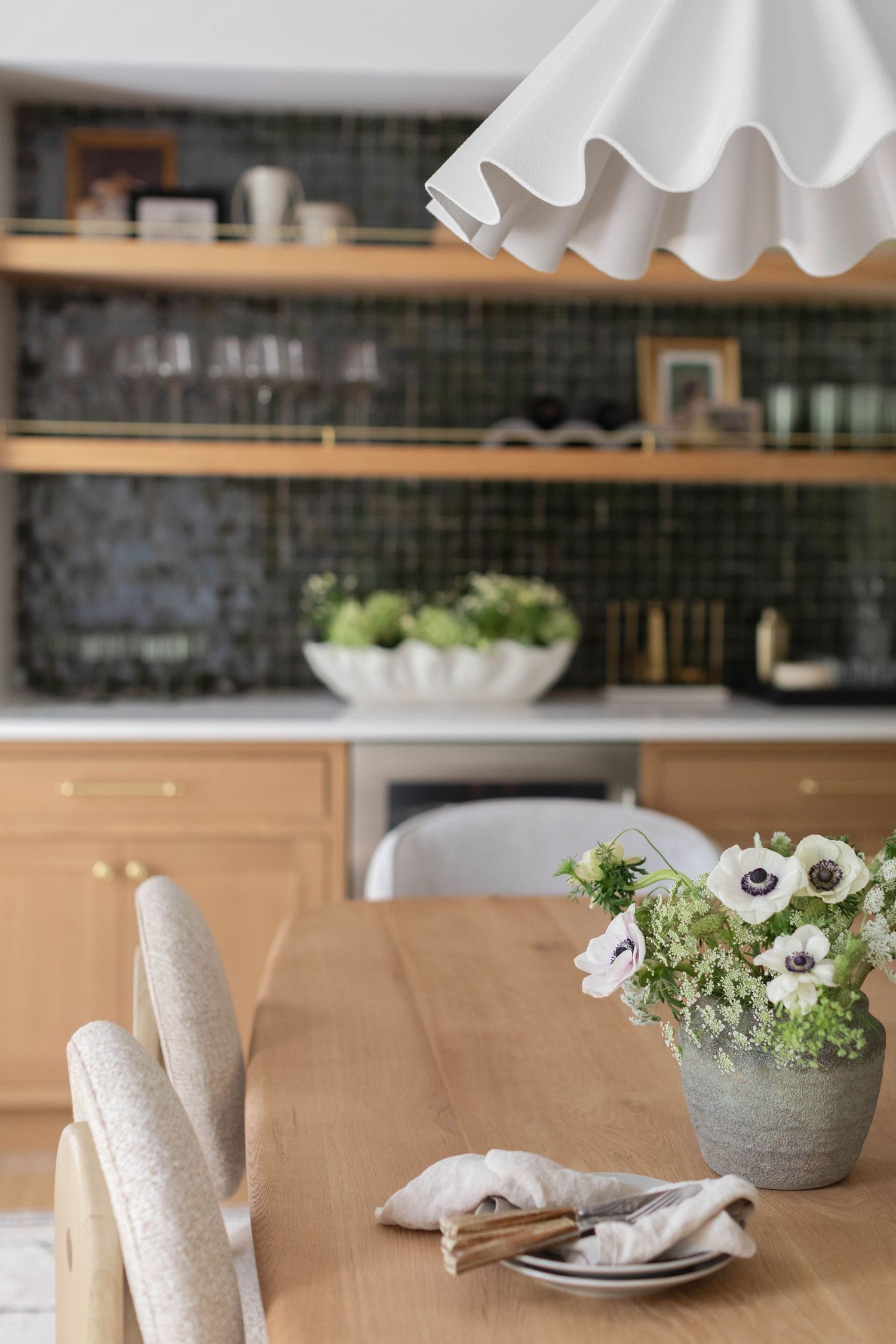 White ceramic dishes and floral arrangements create an elegant table setting with rustic green tile backsplash in background.