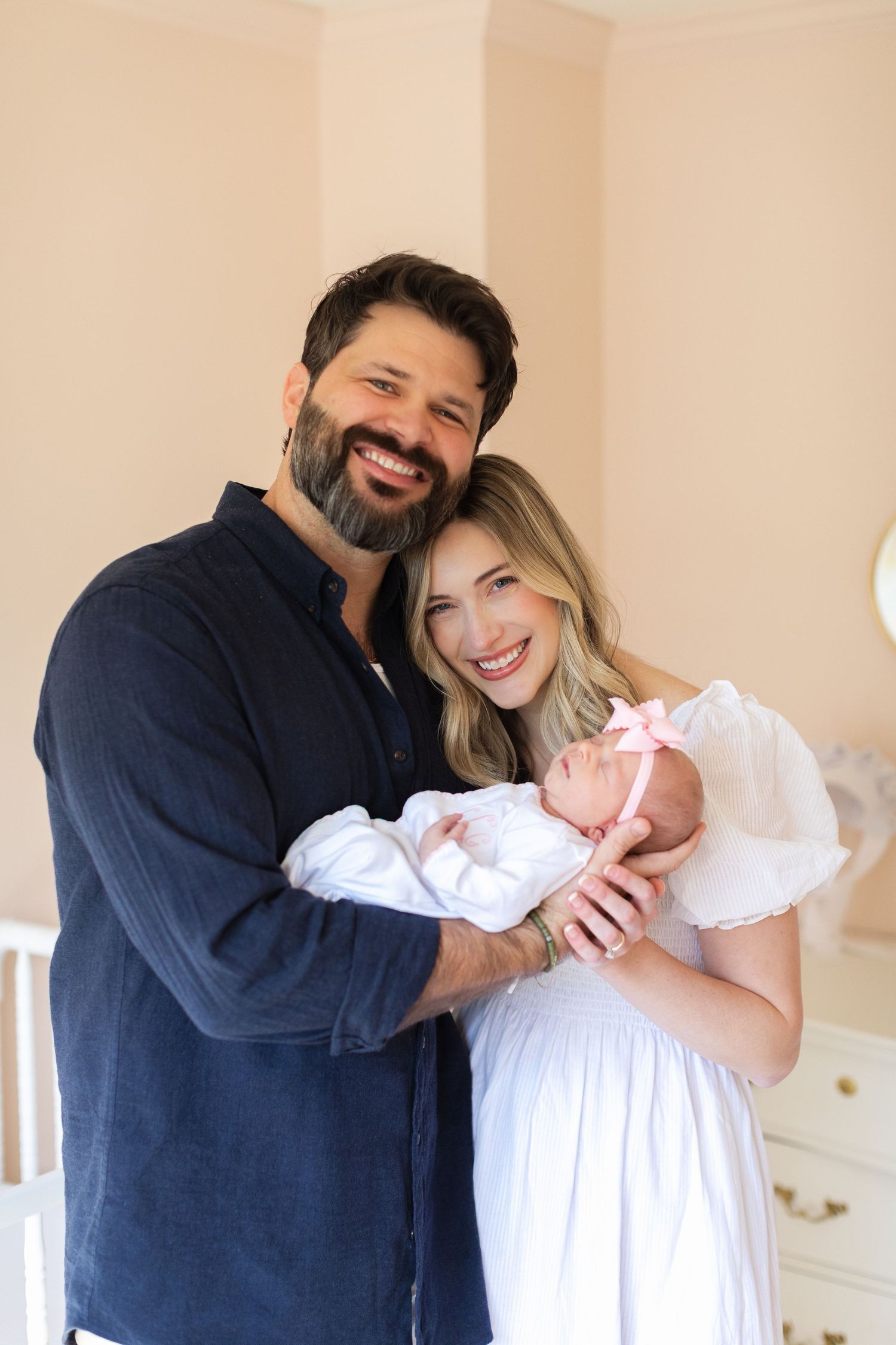 Happy family of three posing together in nursery with white furniture.