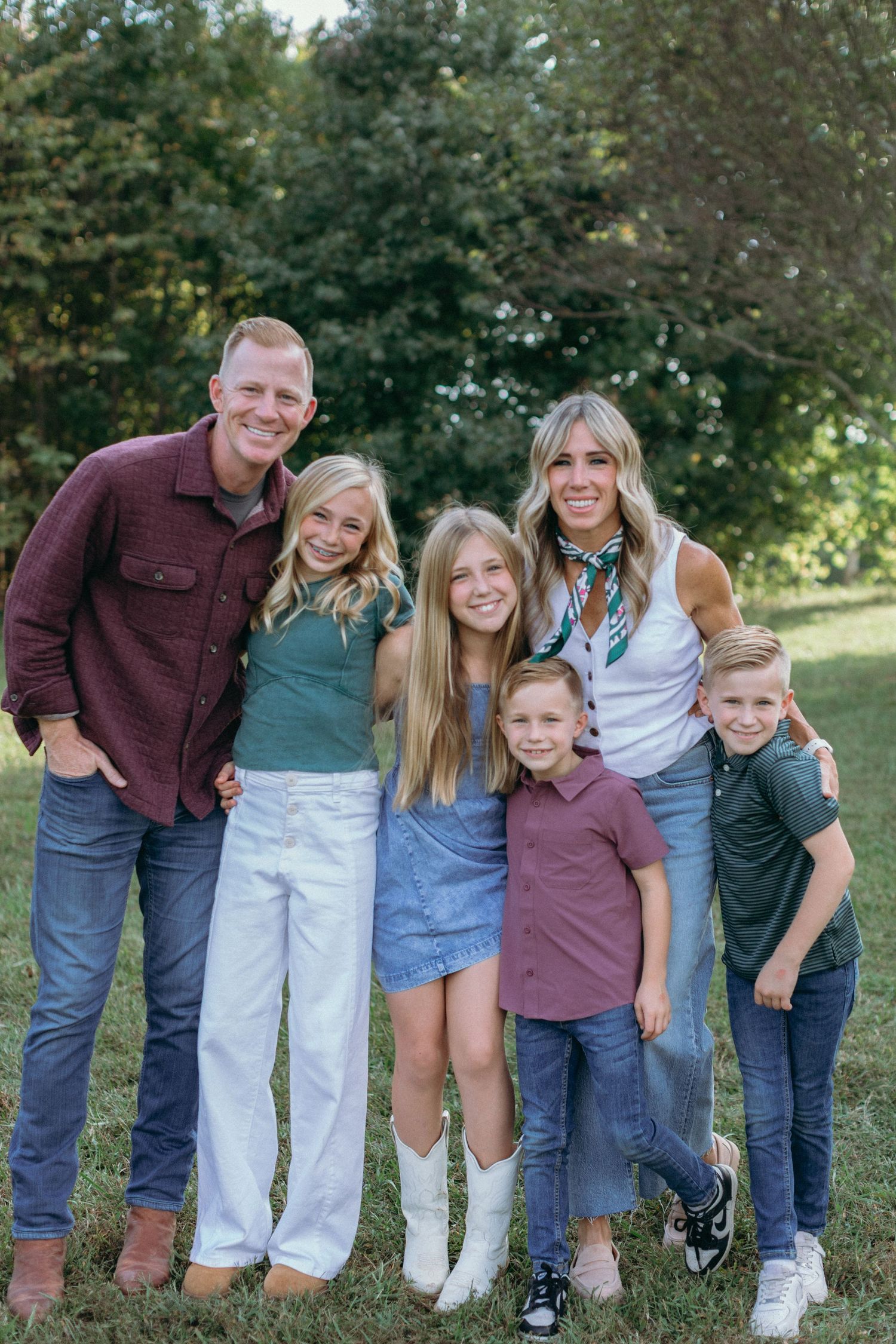 A family group poses together outdoors in coordinated burgundy and blue outfits against a natural background.