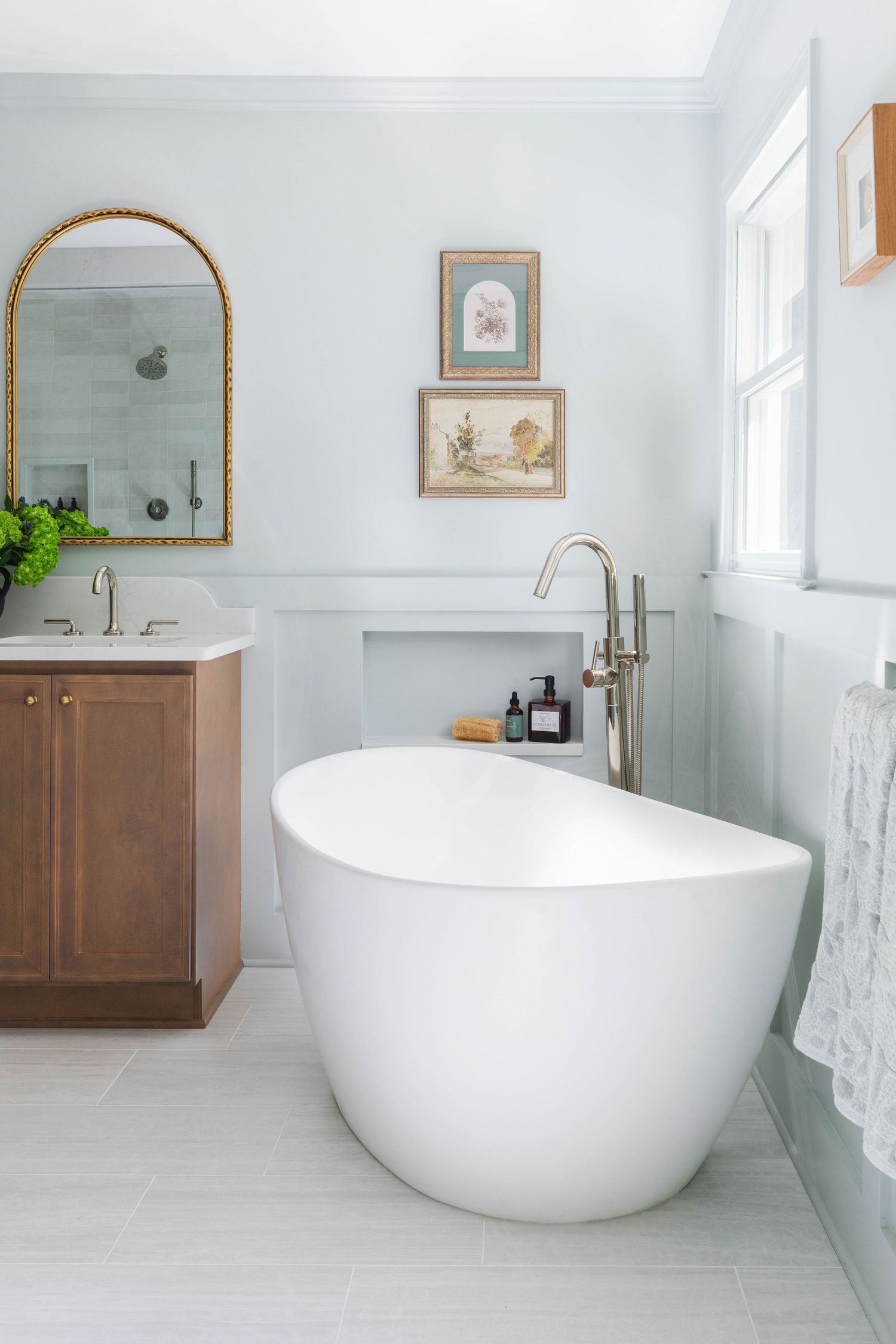 Elegant bathroom with freestanding tub, arched mirror, and wood vanity.