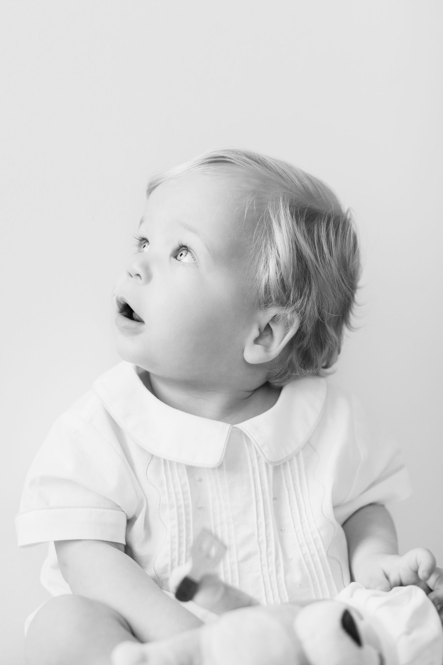 Black and white portrait of baby in white outfit looking up with wonder.