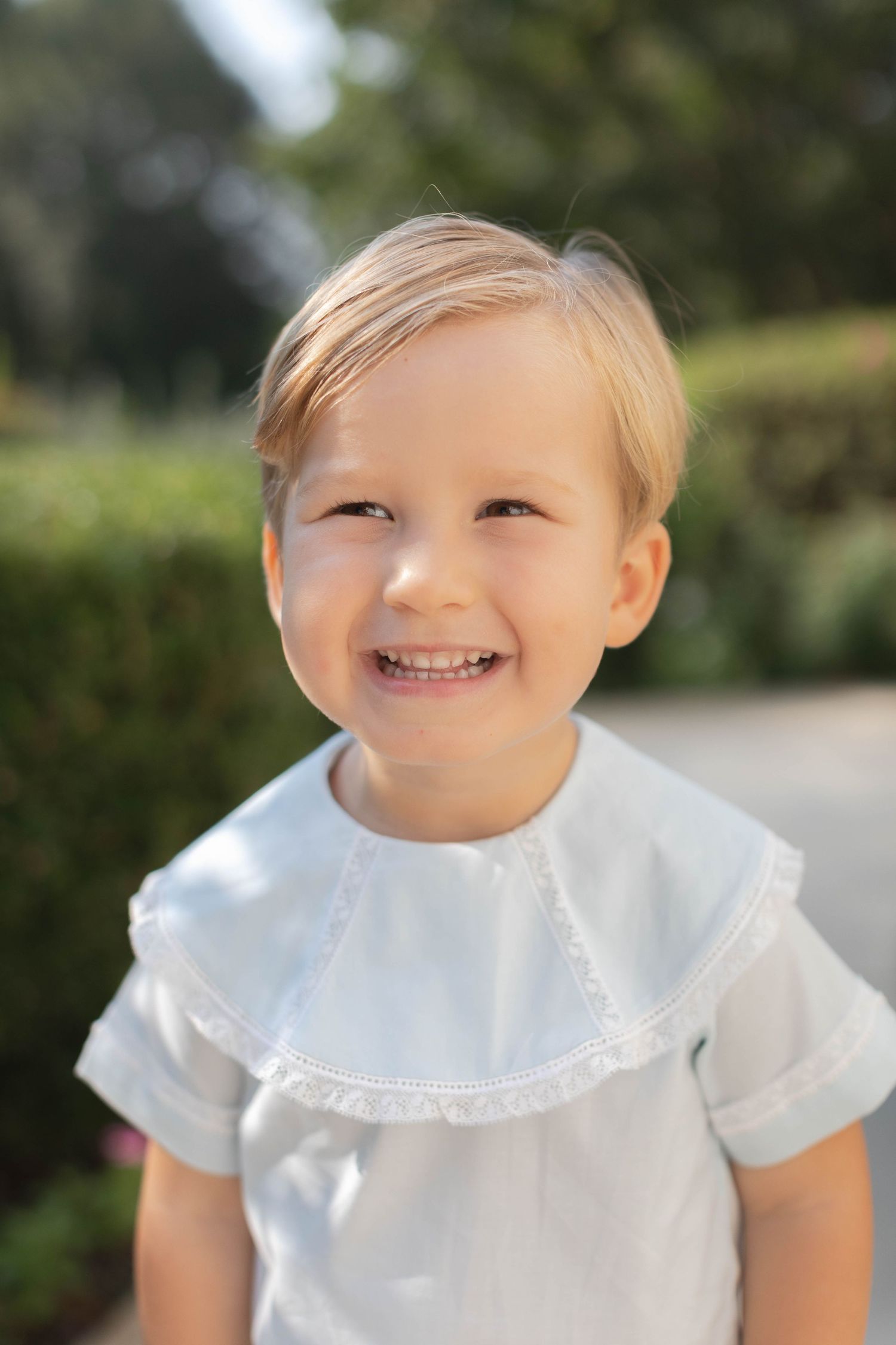 Young child wearing a classic white dress with peter pan collar in bright natural light.
