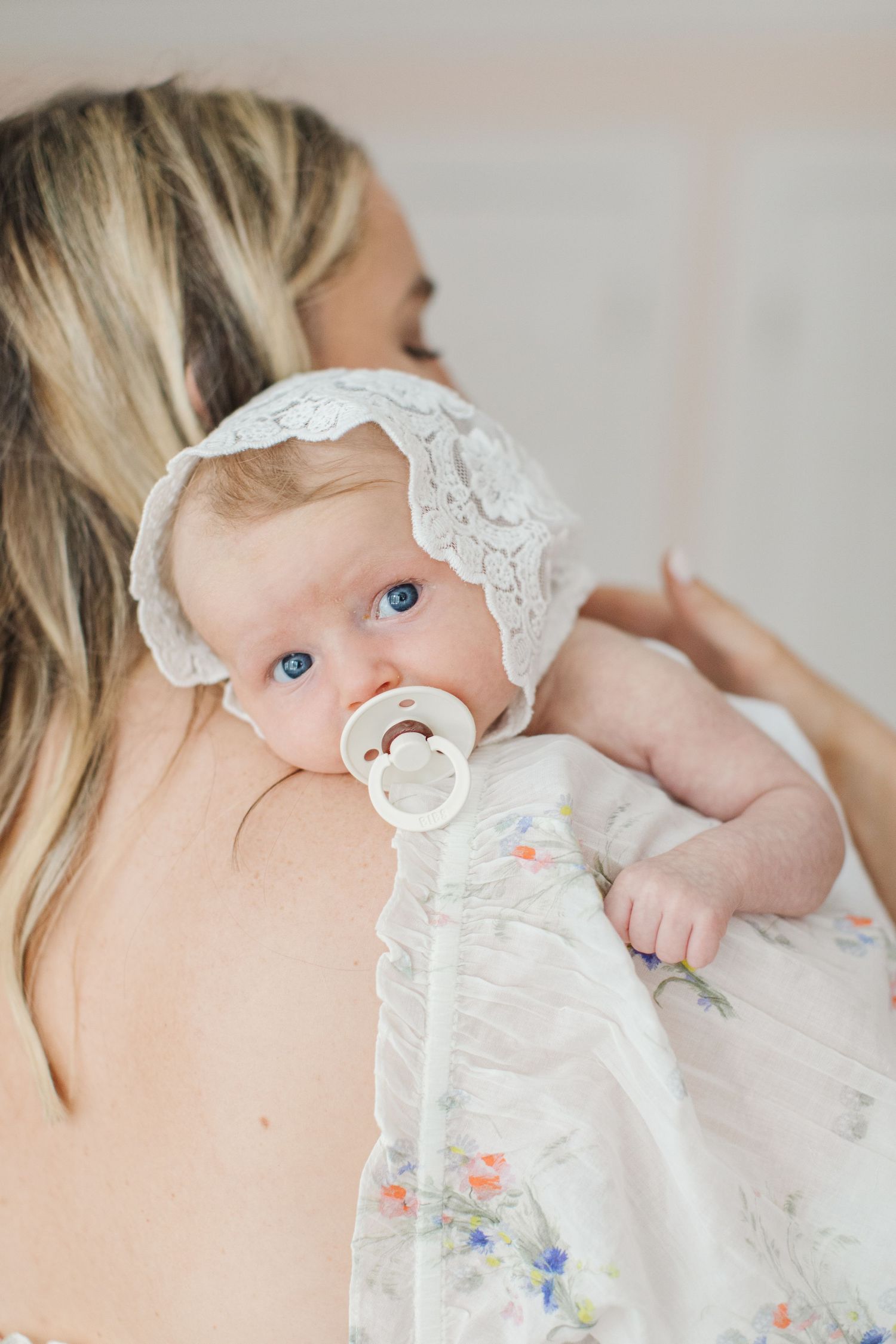 Baby wearing lace bonnet and pacifier in delicate floral outfit.