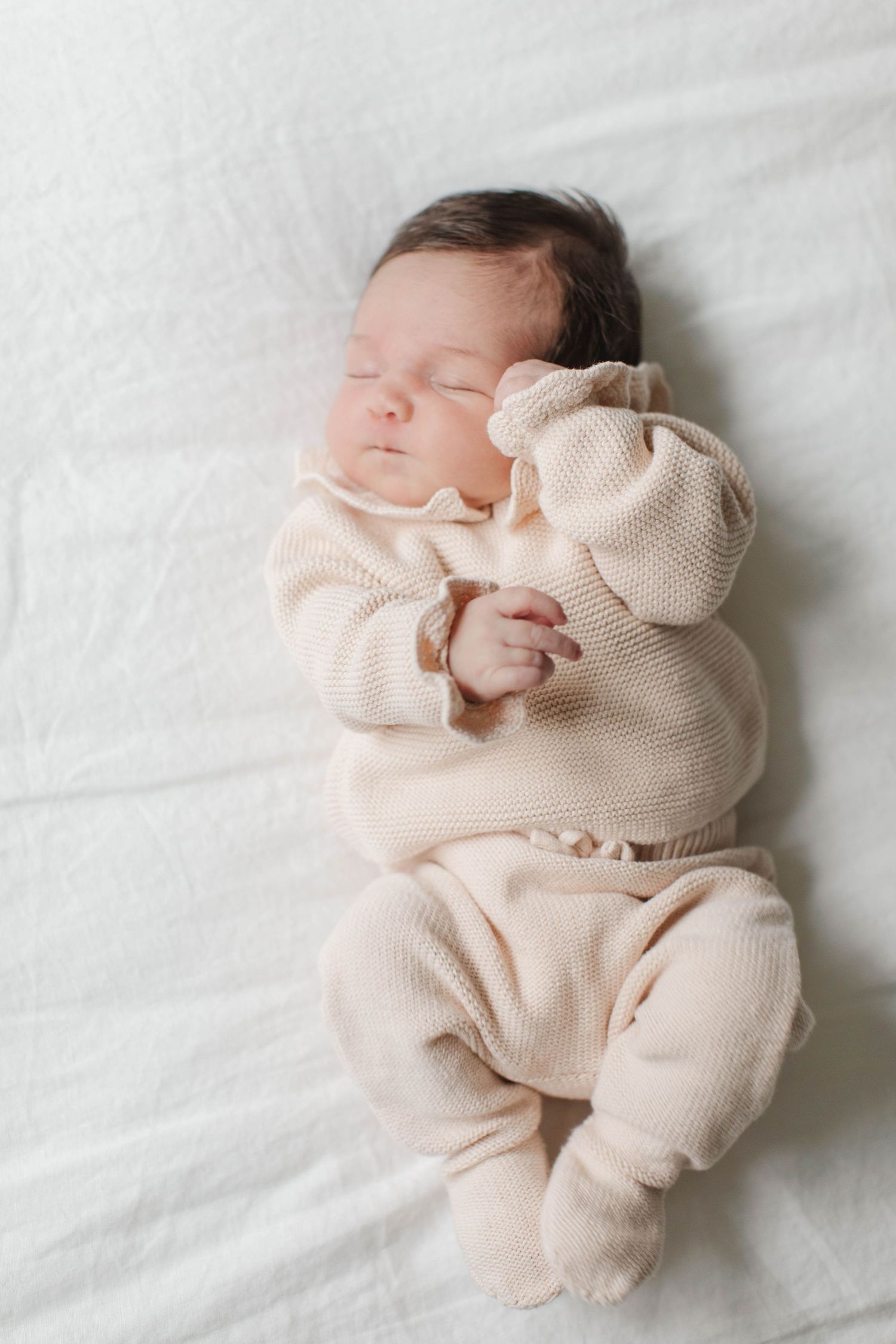 Peaceful sleeping newborn wearing cozy beige knit outfit on white background.