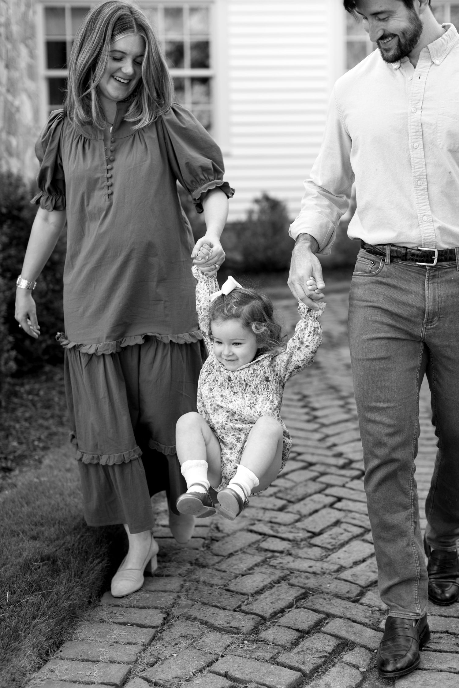 Black and white photos show a toddler learning to walk while holding hands with adults on a stone path.