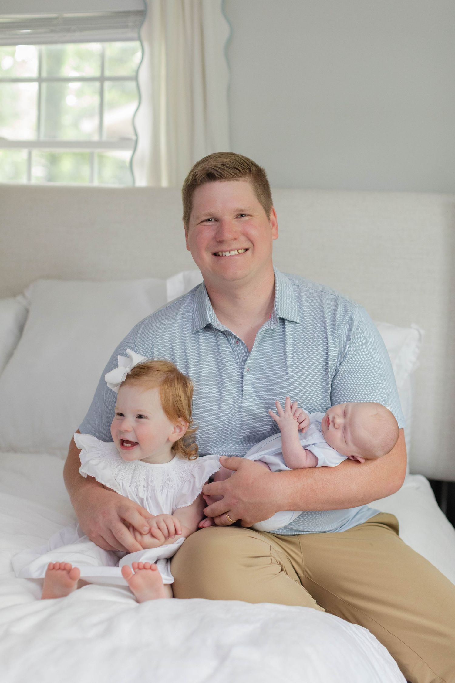A heartwarming family moment captured in bright natural light as they sit together on a white couch.