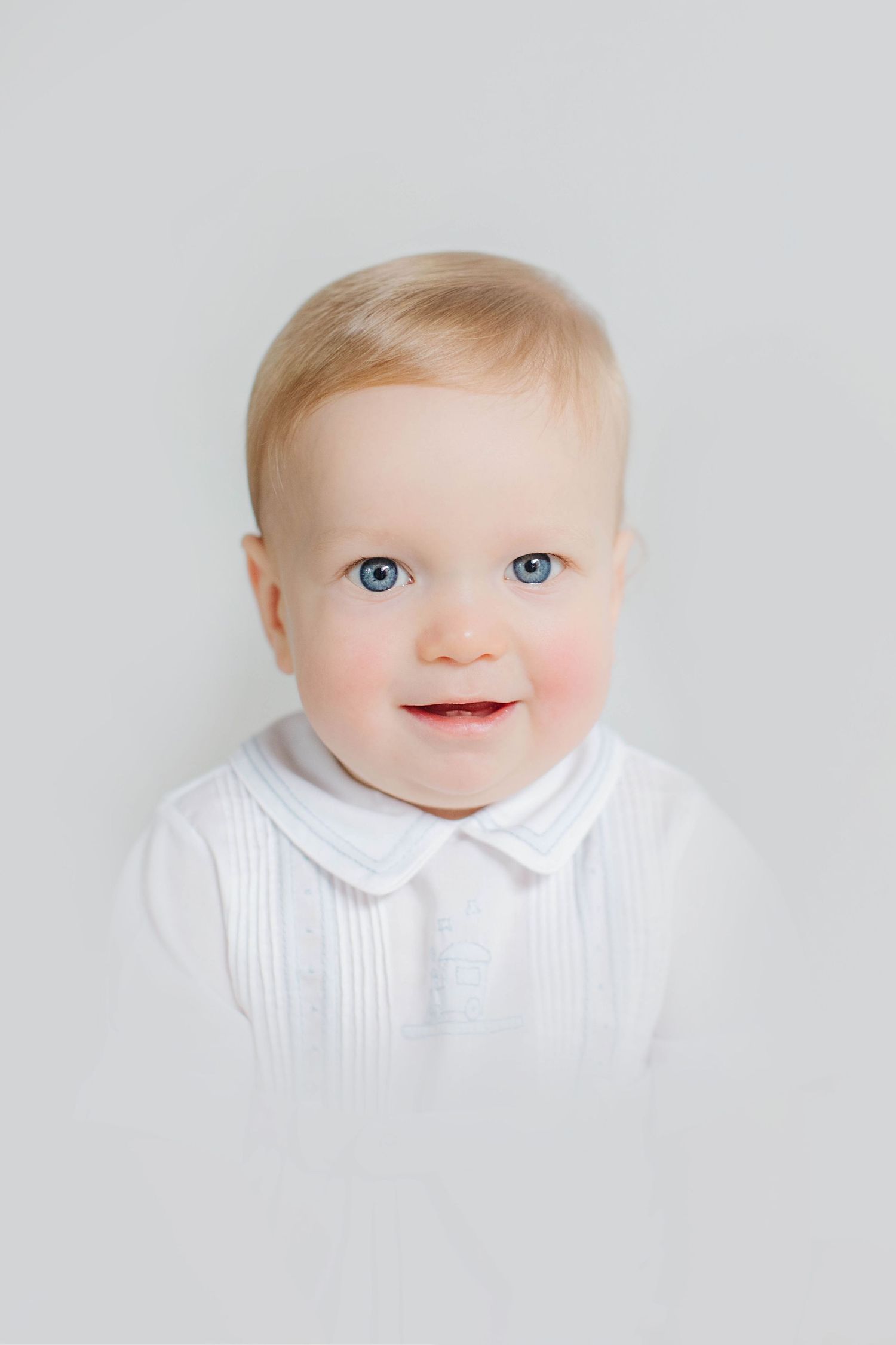 Adorable baby in white collared outfit smiles brightly in series of four close-up portraits.