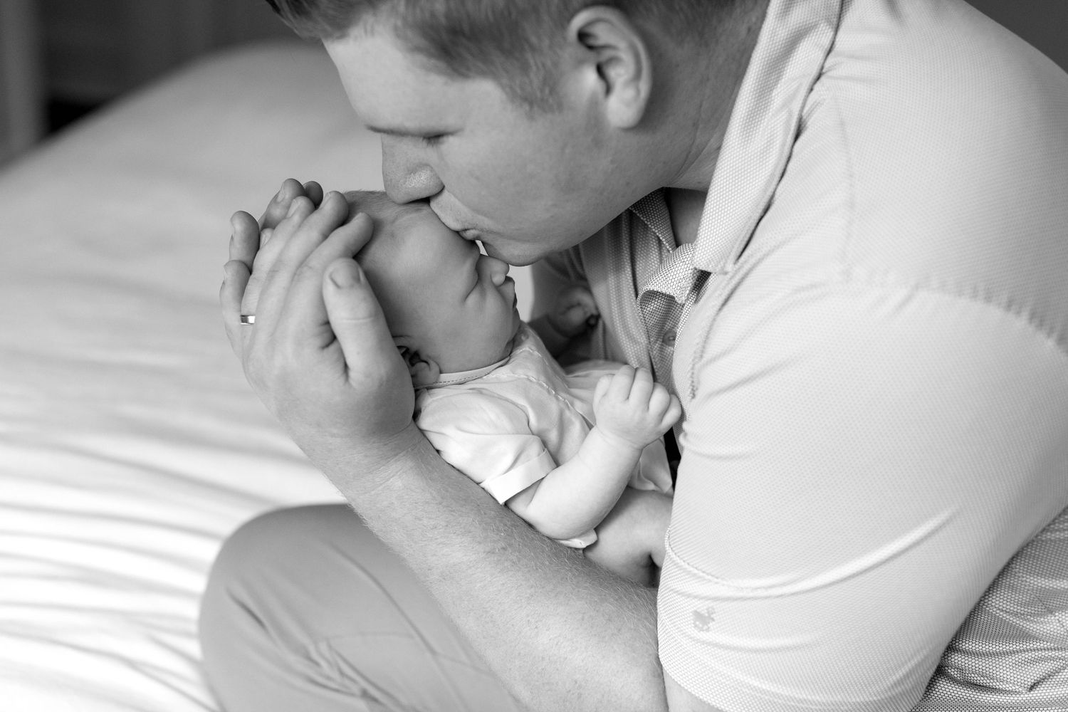 Intimate black and white portrait of parent tenderly holding sleeping newborn on bed.