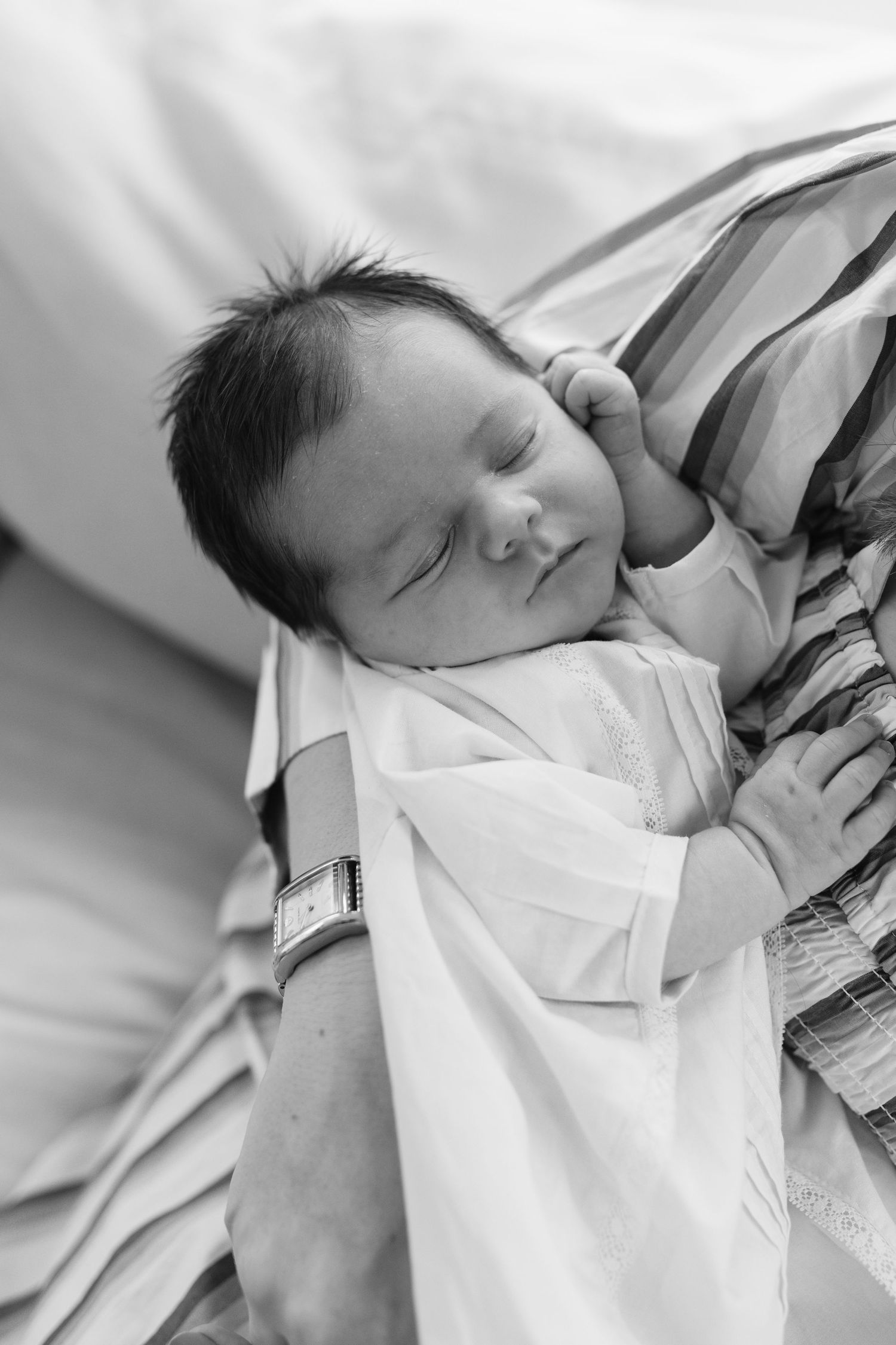 Black and white photo series of a sleeping newborn baby wearing a white outfit.
