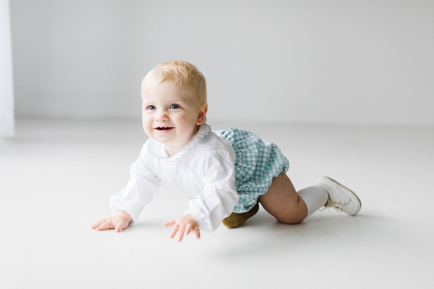 Baby in white outfit crawls and laughs on light gray floor in minimalist setting.