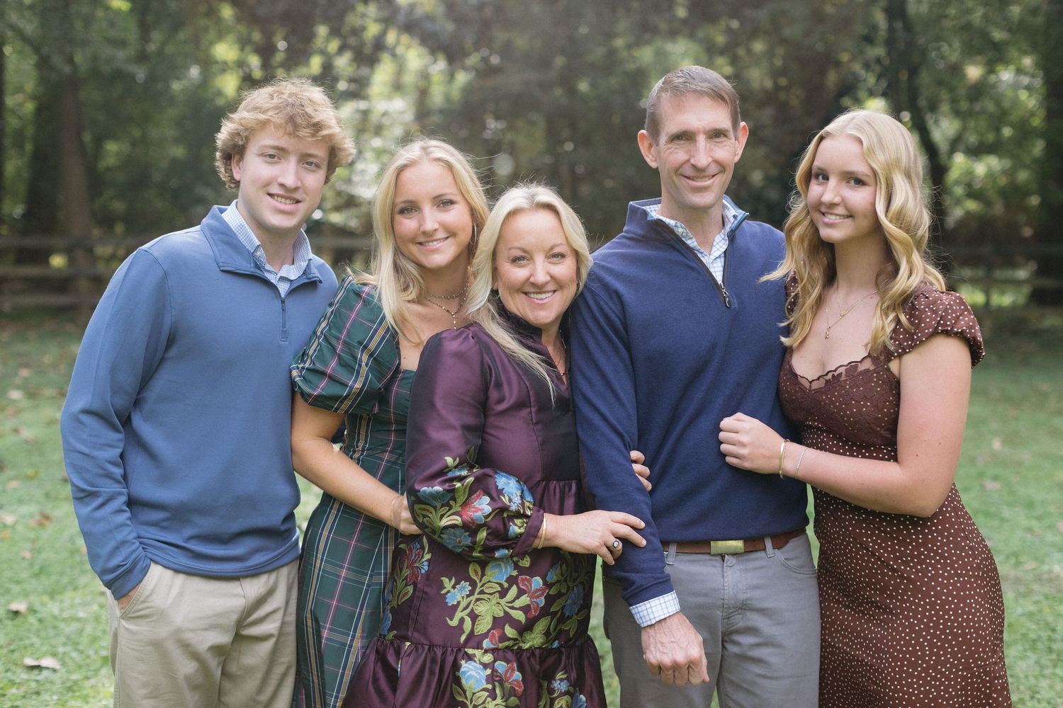 A group of five people wearing coordinated blue and purple outfits pose together outdoors for a family portrait.