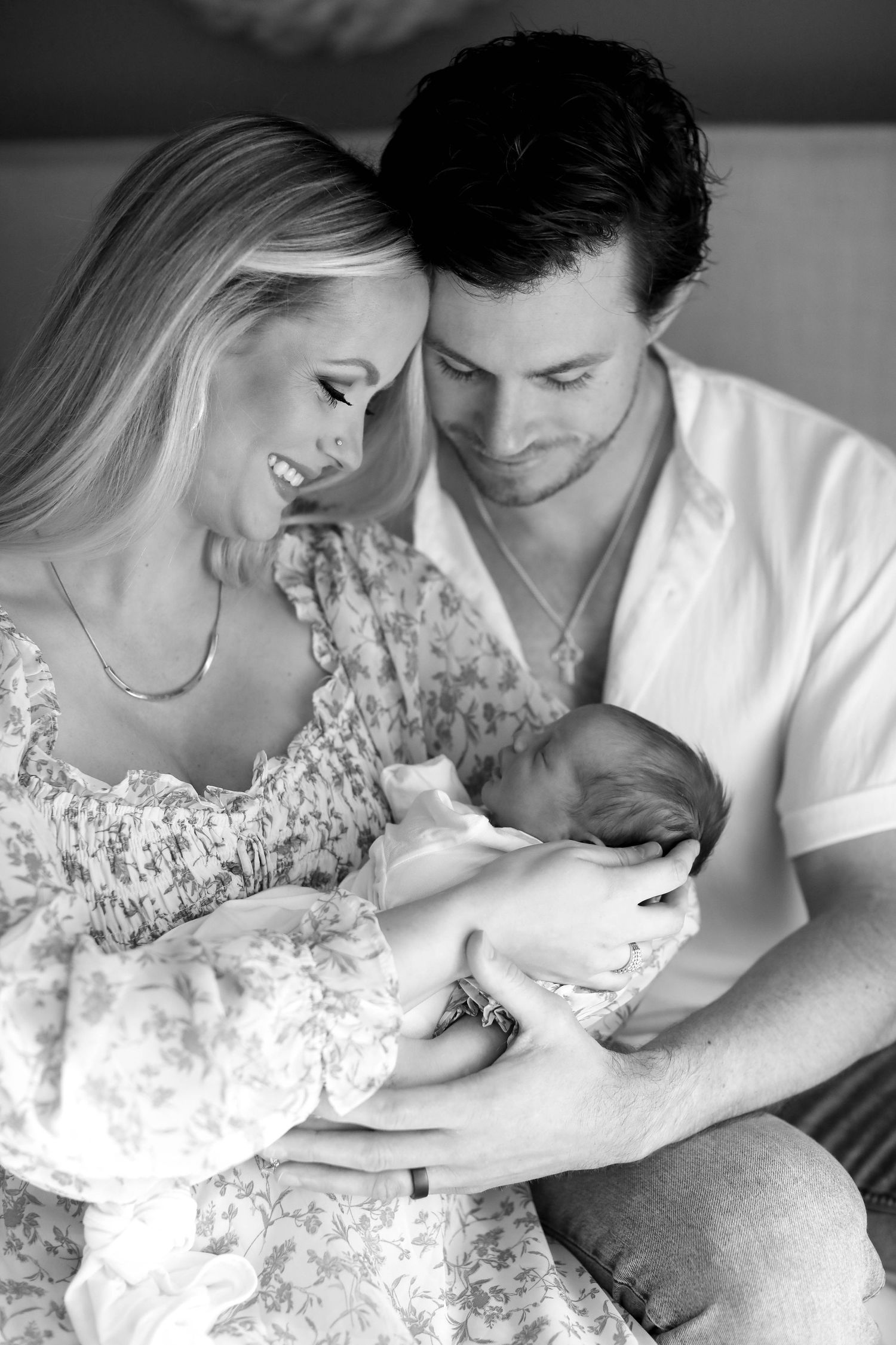 An intimate black and white portrait of new parents cradling their newborn baby together.