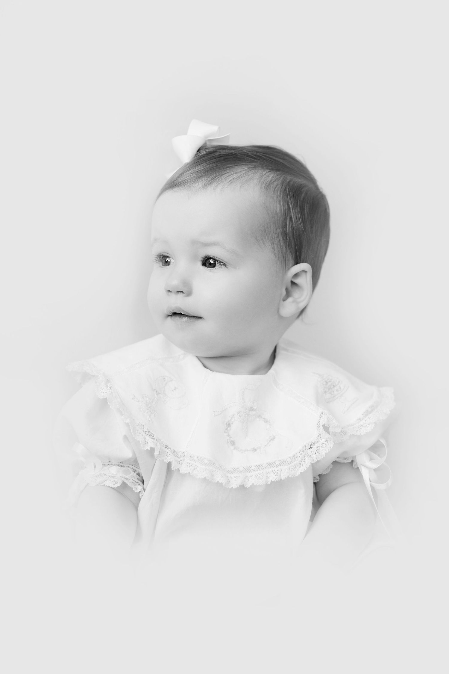 Three black and white artistic portraits of a baby in white lace dress against light background.