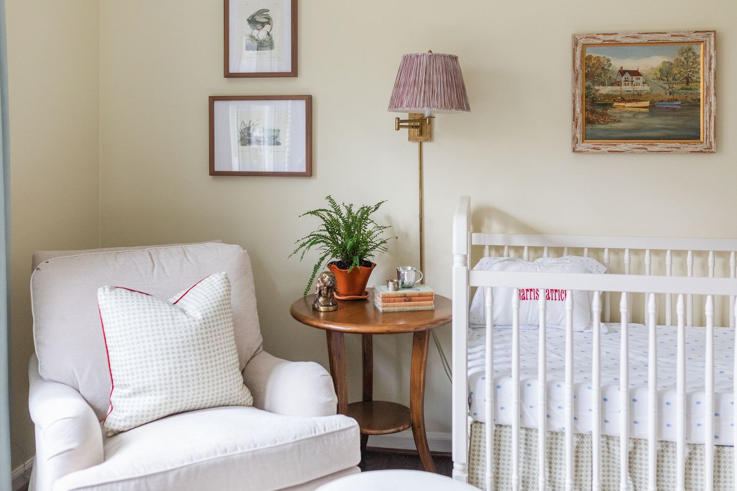 A cozy nursery room with white crib, soft textiles, and neutral decor featuring wall art and potted plants.