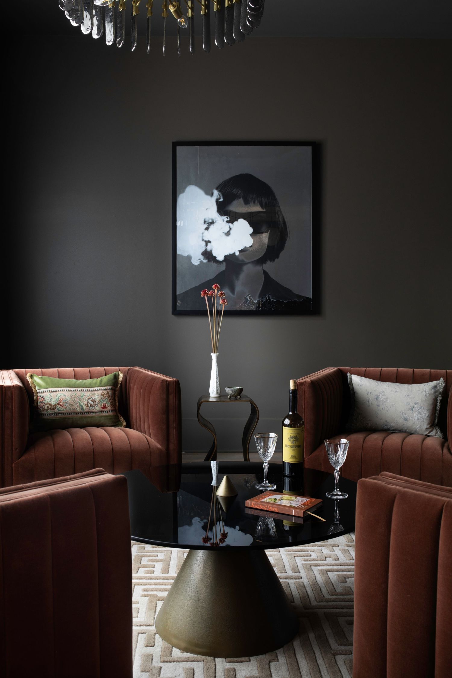 Dark moody living room with velvet rust sofas, black coffee table, wine glasses, and framed smoke portrait art on charcoal wall.