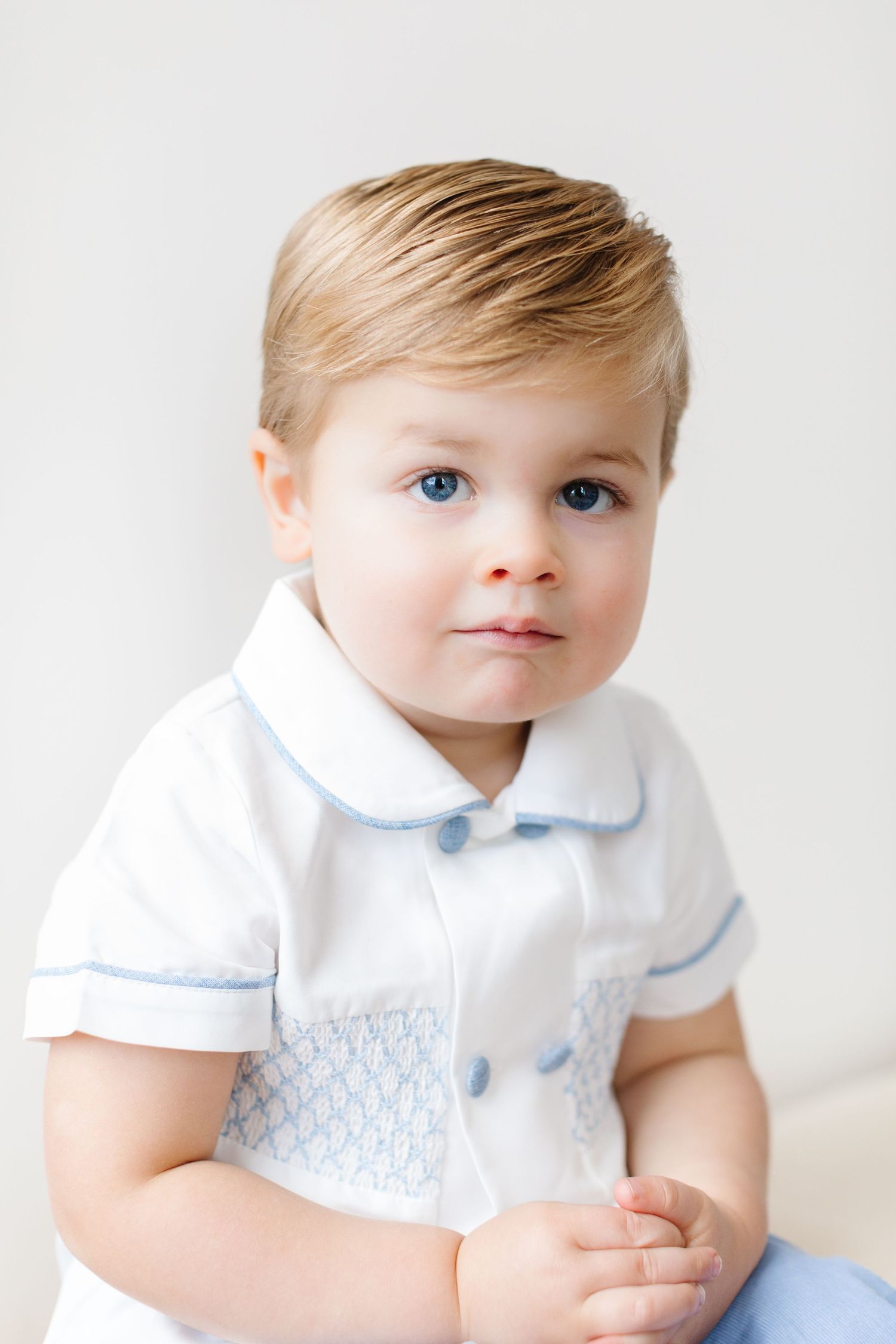 A small child wearing a white outfit with blue details poses against a bright white background.