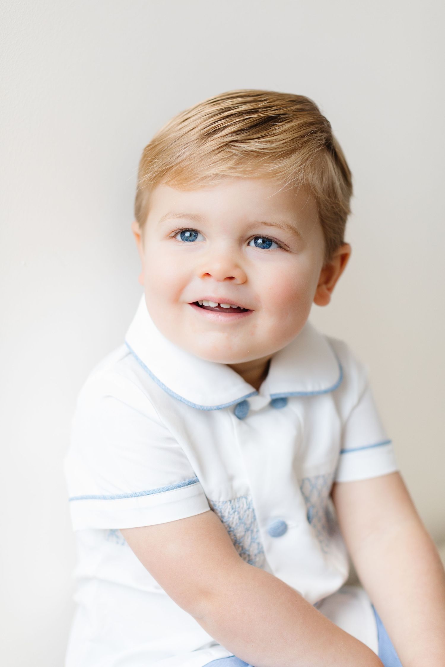 Sweet baby in white collared outfit with light blue trim smiles while looking to the side.