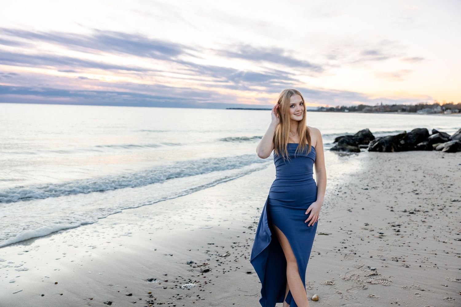 Woman in blue dress walks along peaceful beach at sunset with waves rolling in.