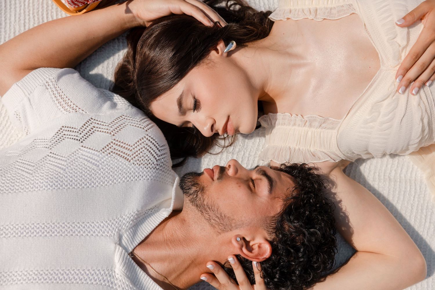 Intimate couple lying together on white bedding in a romantic embrace.
