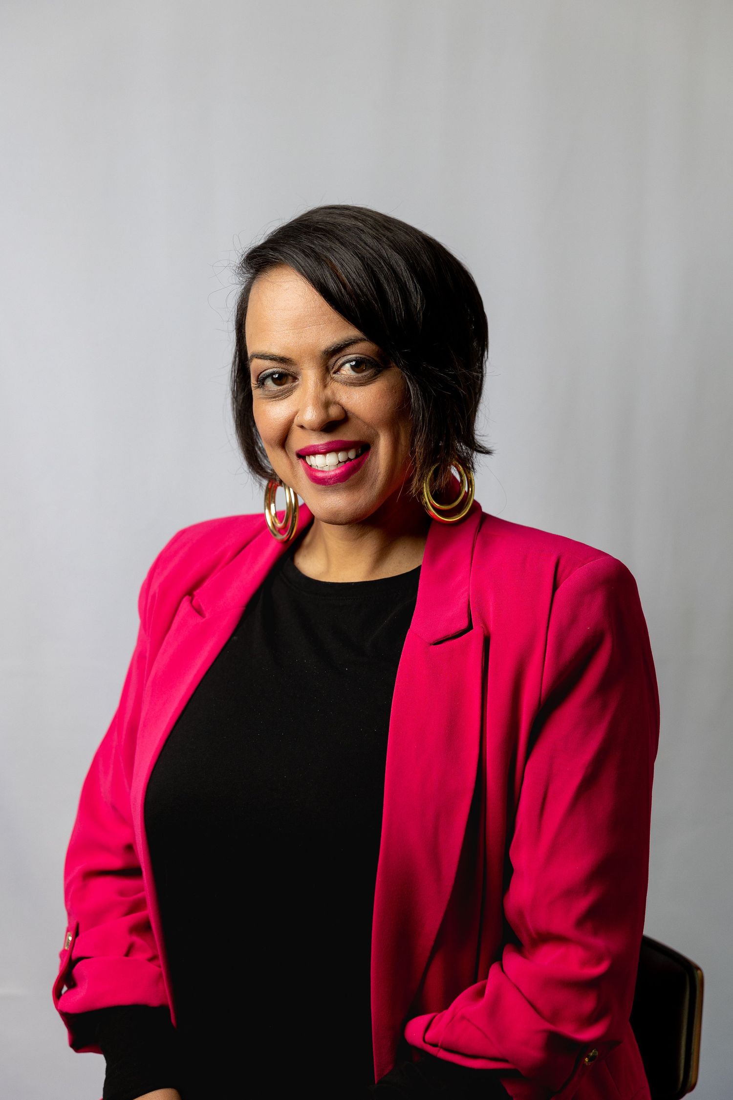 Professional headshots of woman in bright pink blazer against grey background.