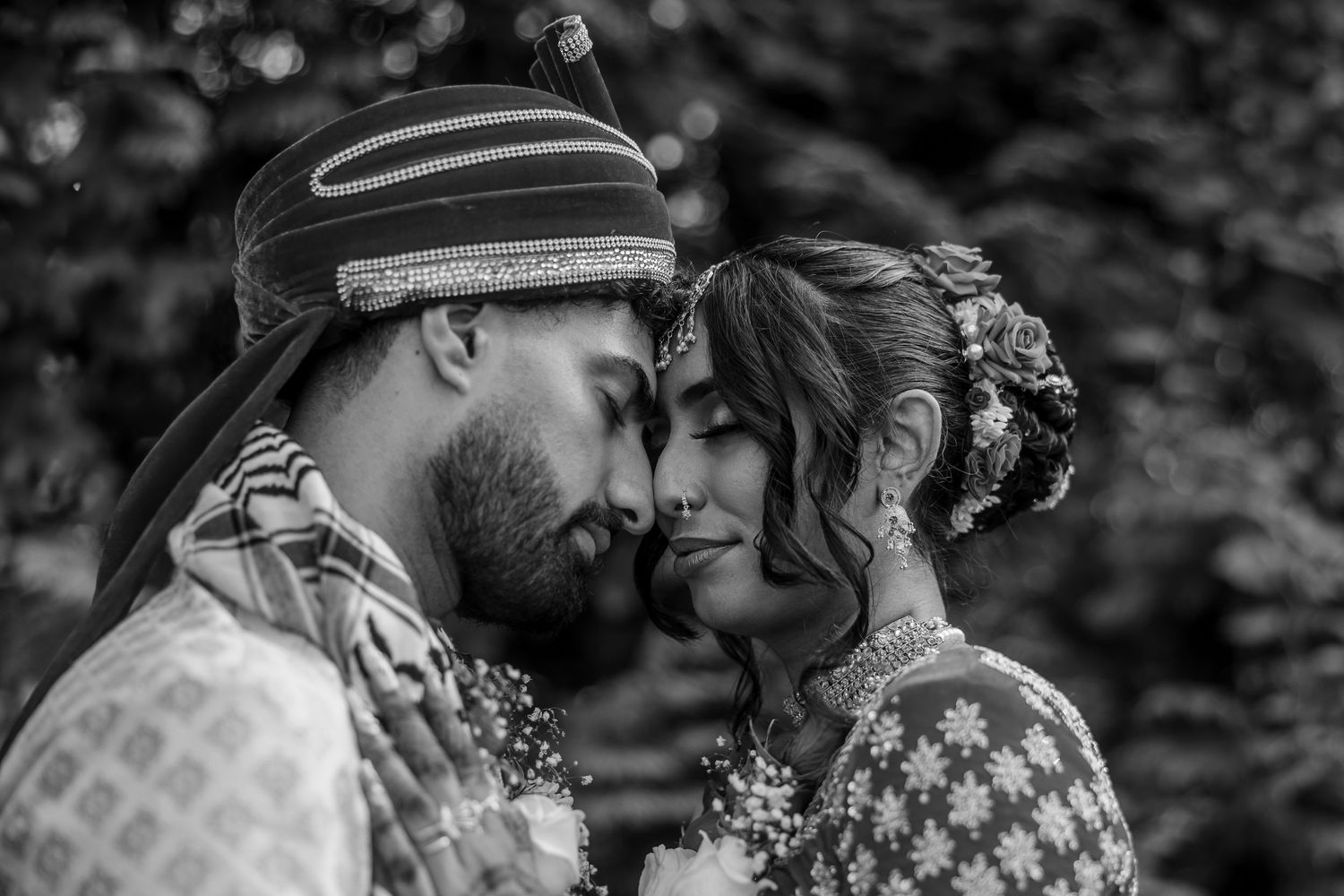 An intimate black and white portrait of a couple in traditional wedding attire sharing a tender moment.