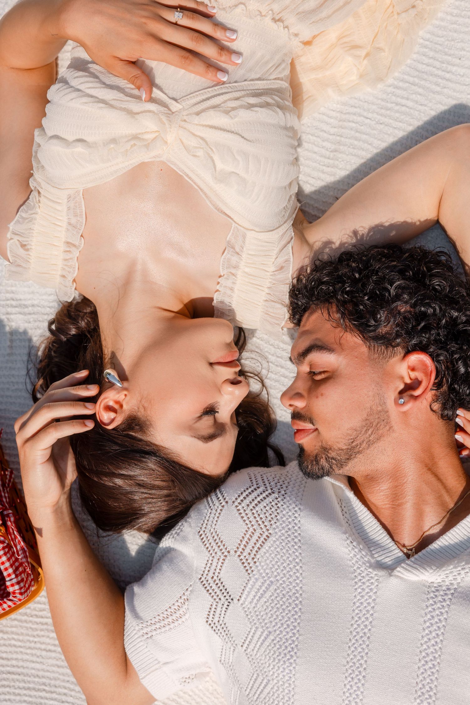 Couple sharing tender moments while resting on textured white bedding.