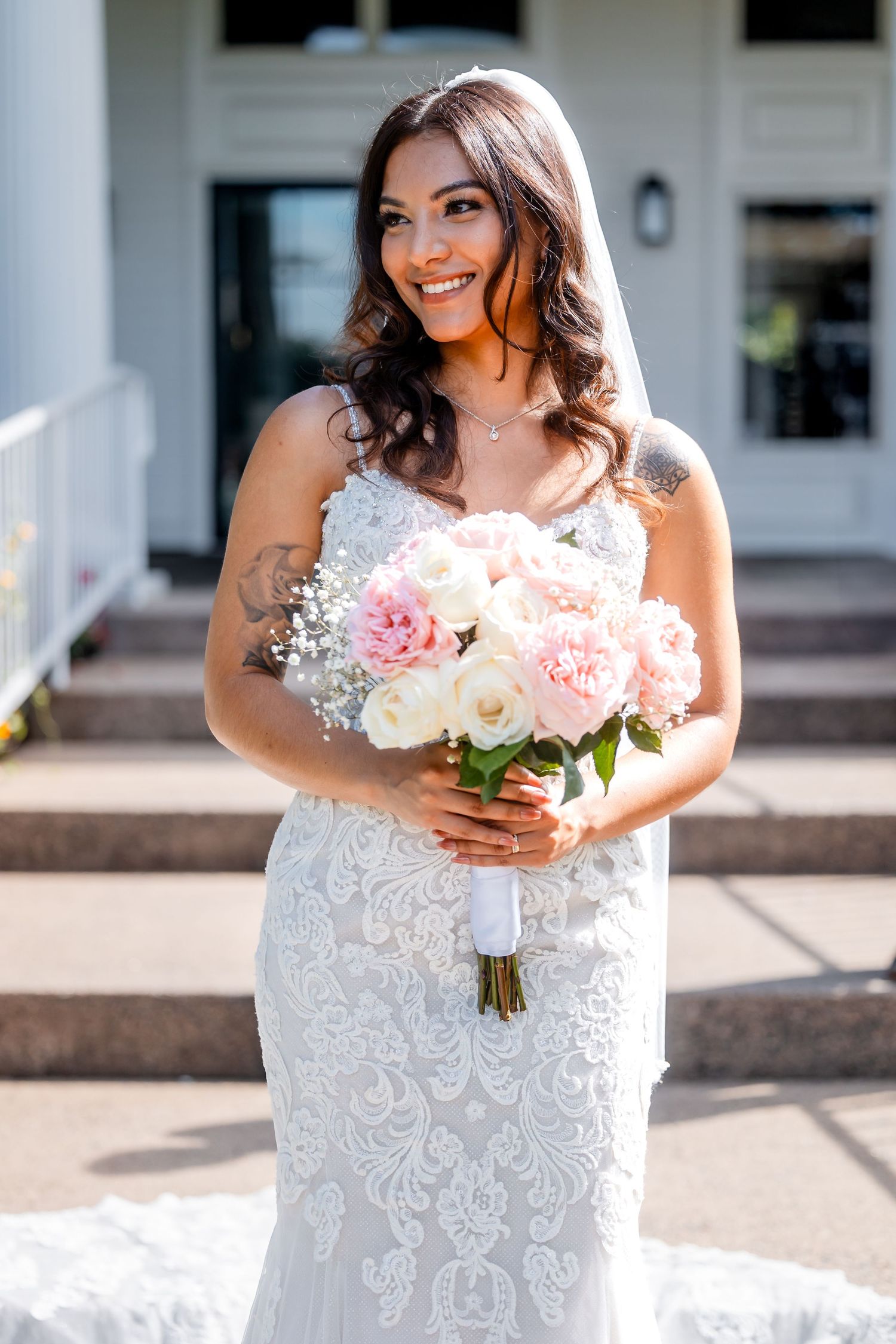 Person in detailed white lace wedding dress holding a bouquet of pink and white flowers.