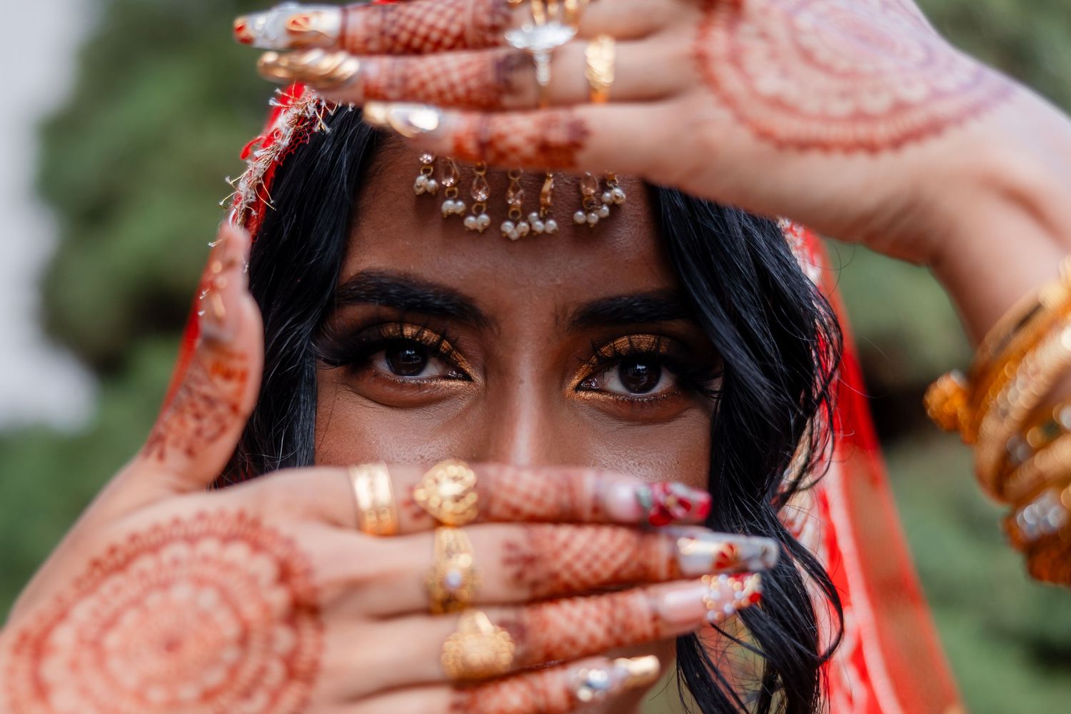 Traditional bridal portrait with henna-decorated hands and ornate jewelry.