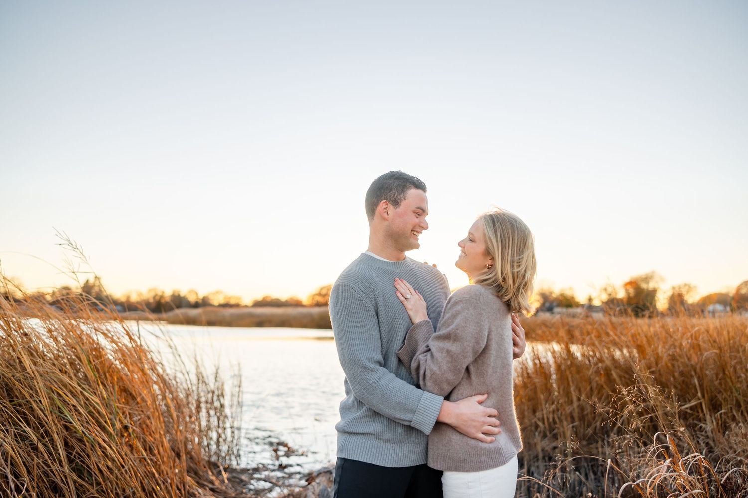 Couple shares tender moment among tall grass during golden sunset by lake.