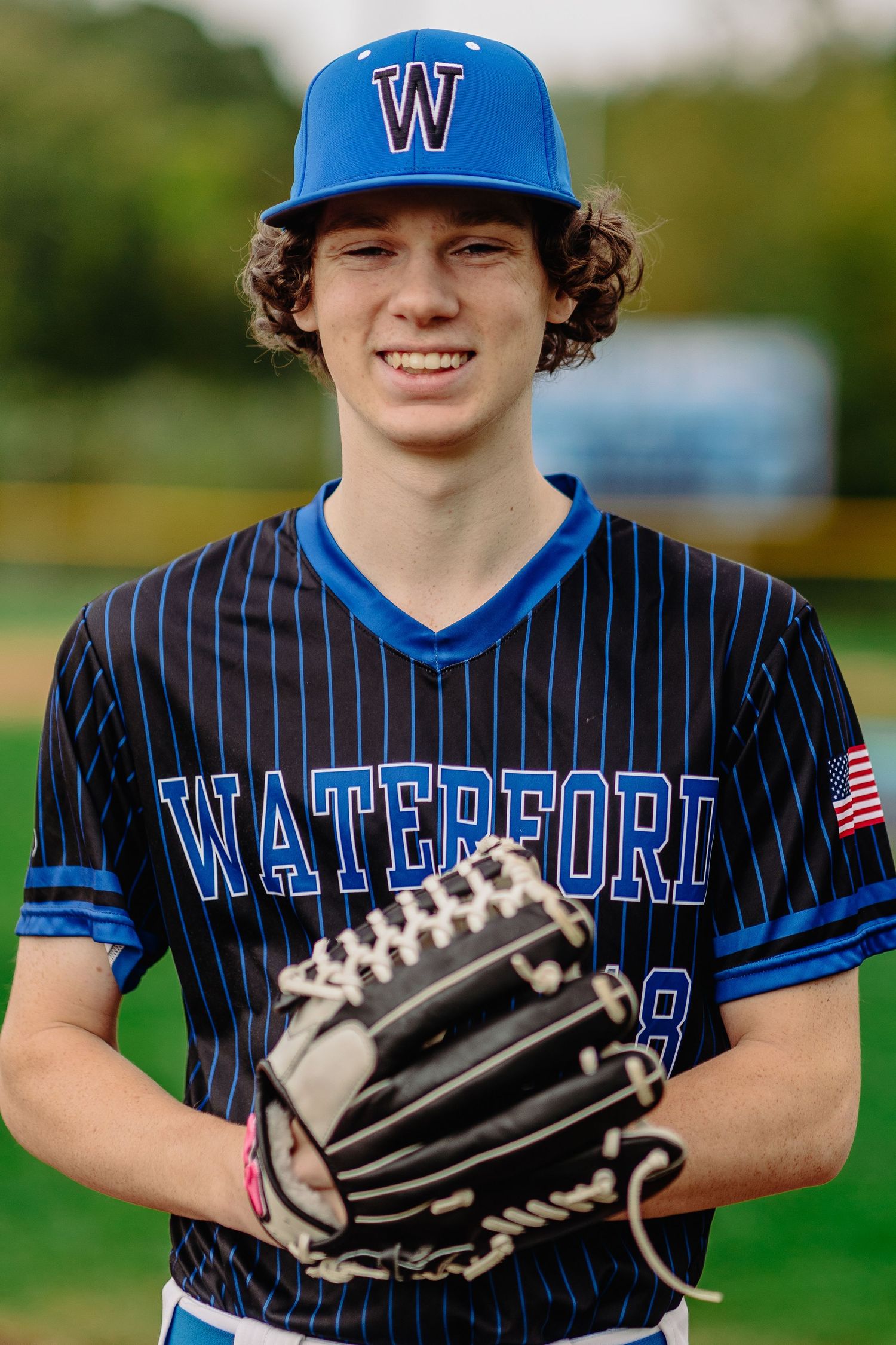 Young baseball player in blue and black pinstriped Waterford uniform holding baseball glove and smiling at camera