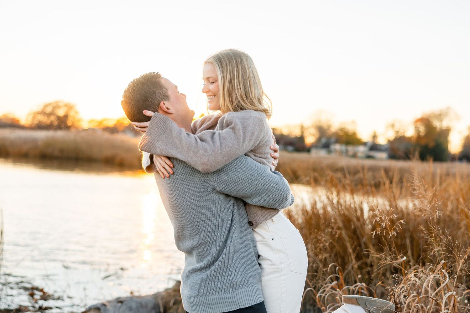Couple embraces during golden hour in autumn field by the water.