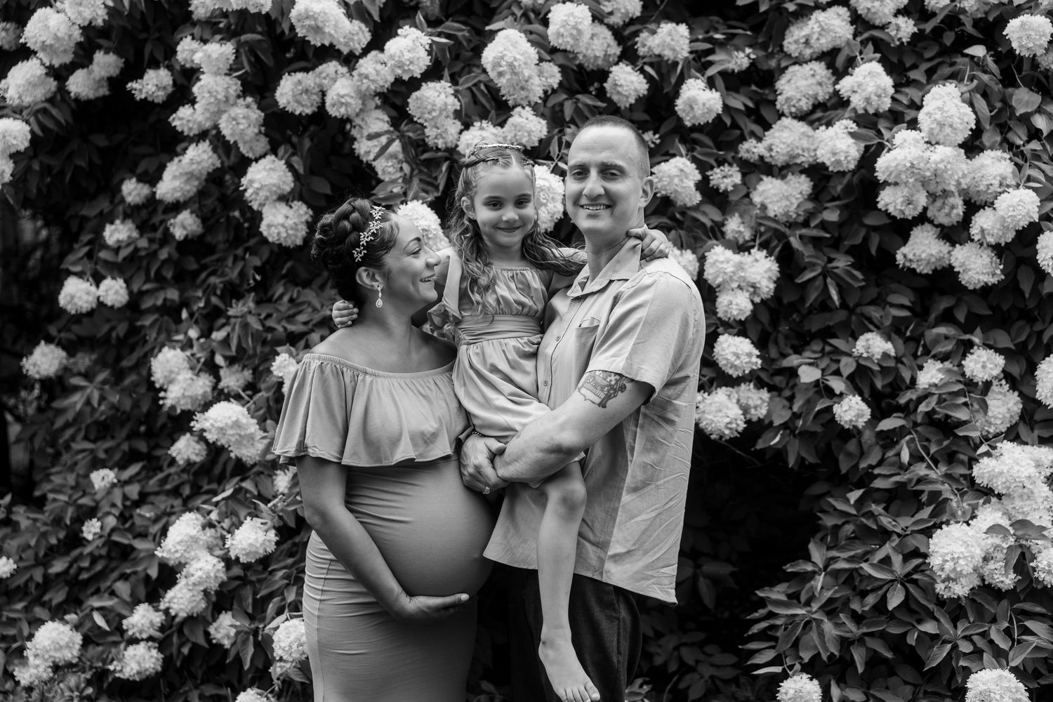 A couple shares intimate moments in a garden setting with white roses in the background.