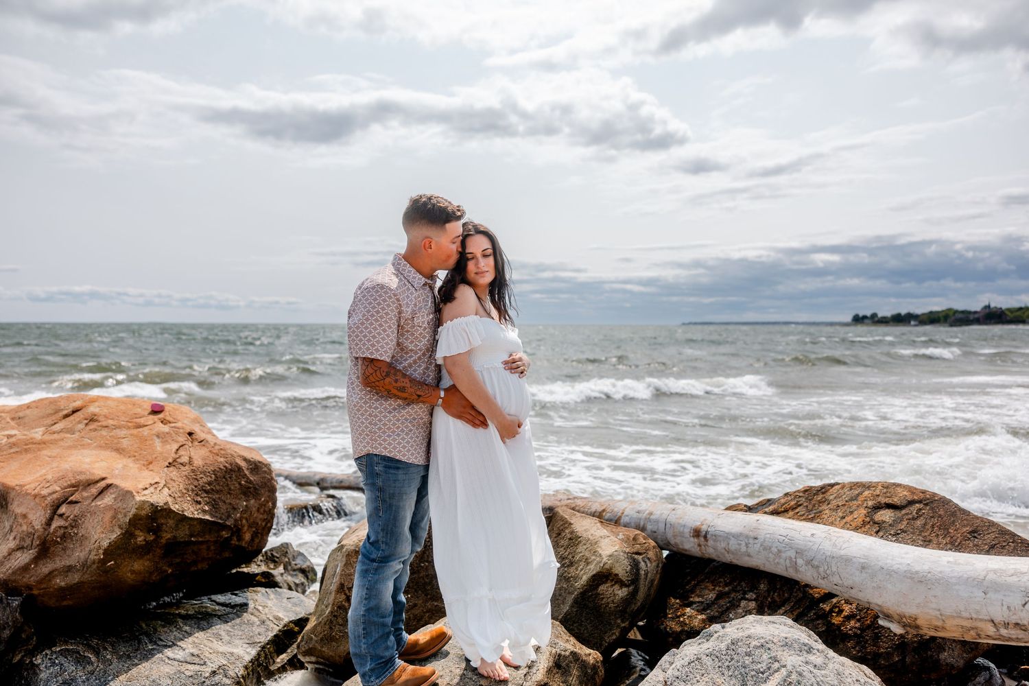 Couple shares intimate moment on rocky beach coastline during cloudy day.