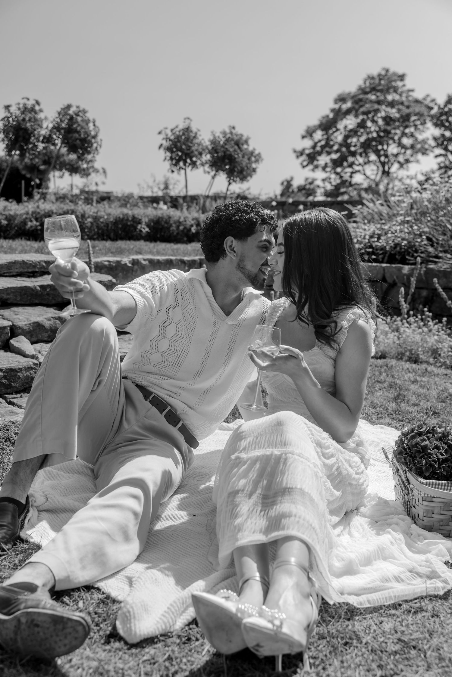 Romantic couple in white clothing lounging on a blanket outdoors on a sunny day.