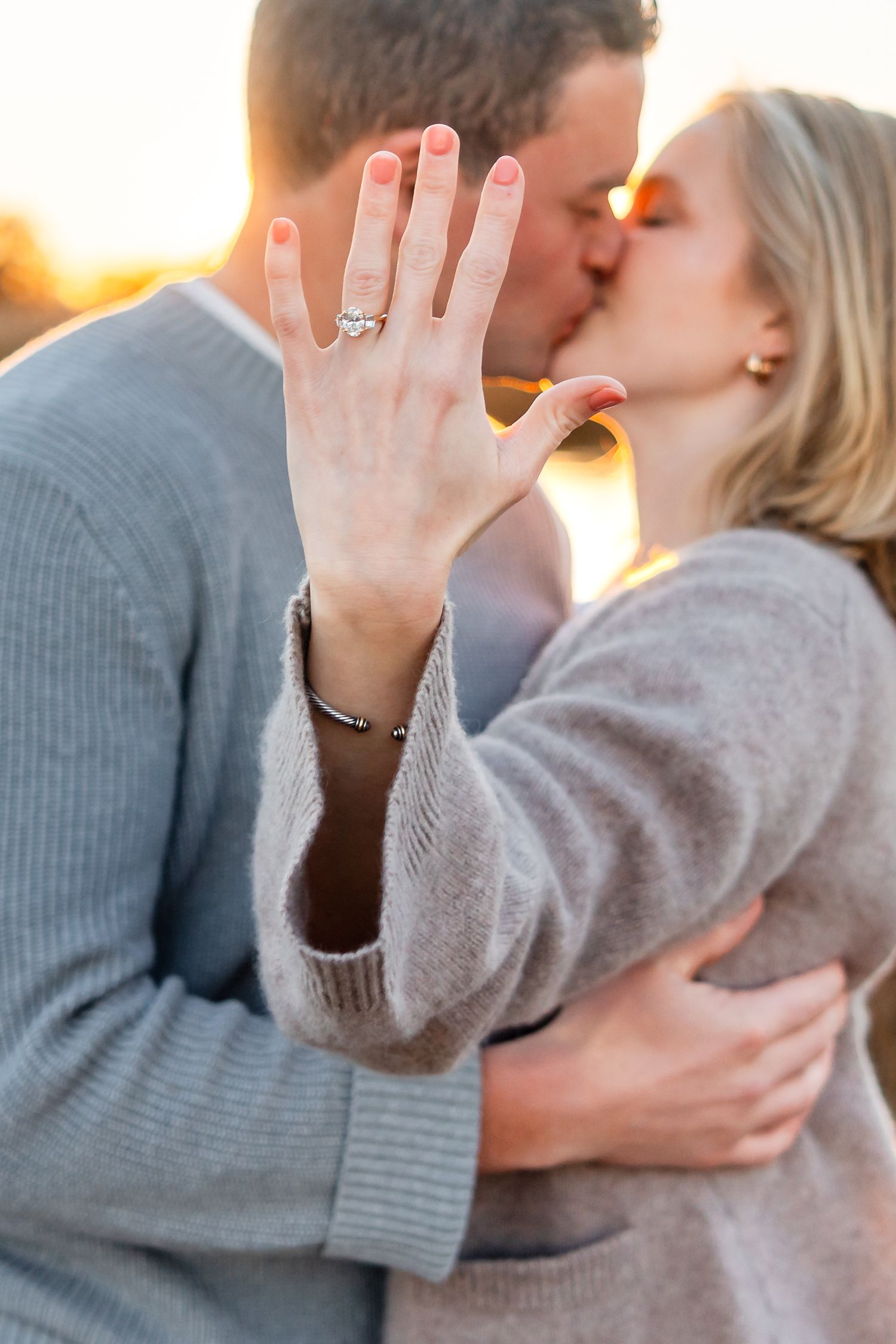Close up of engagement ring as couple shares romantic sunset kiss.