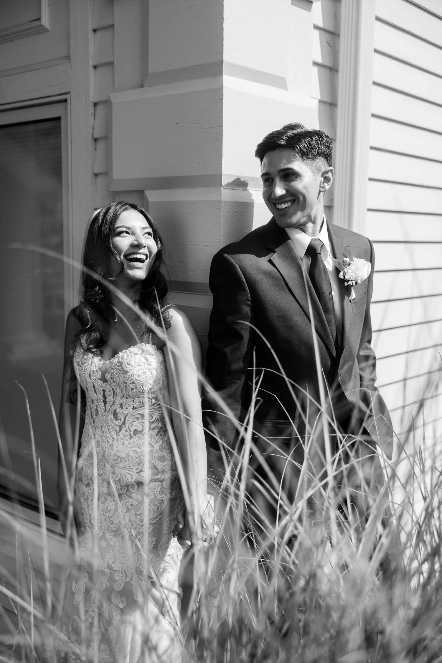 Black and white wedding portraits against a white house with tall grass in the foreground.
