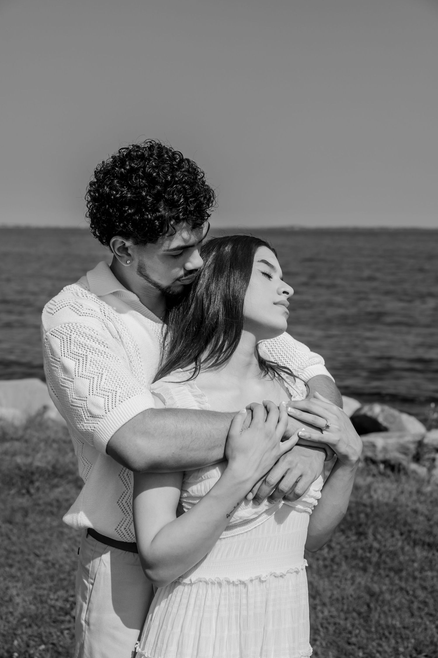 Intimate black and white portrait of a couple embracing by the ocean.