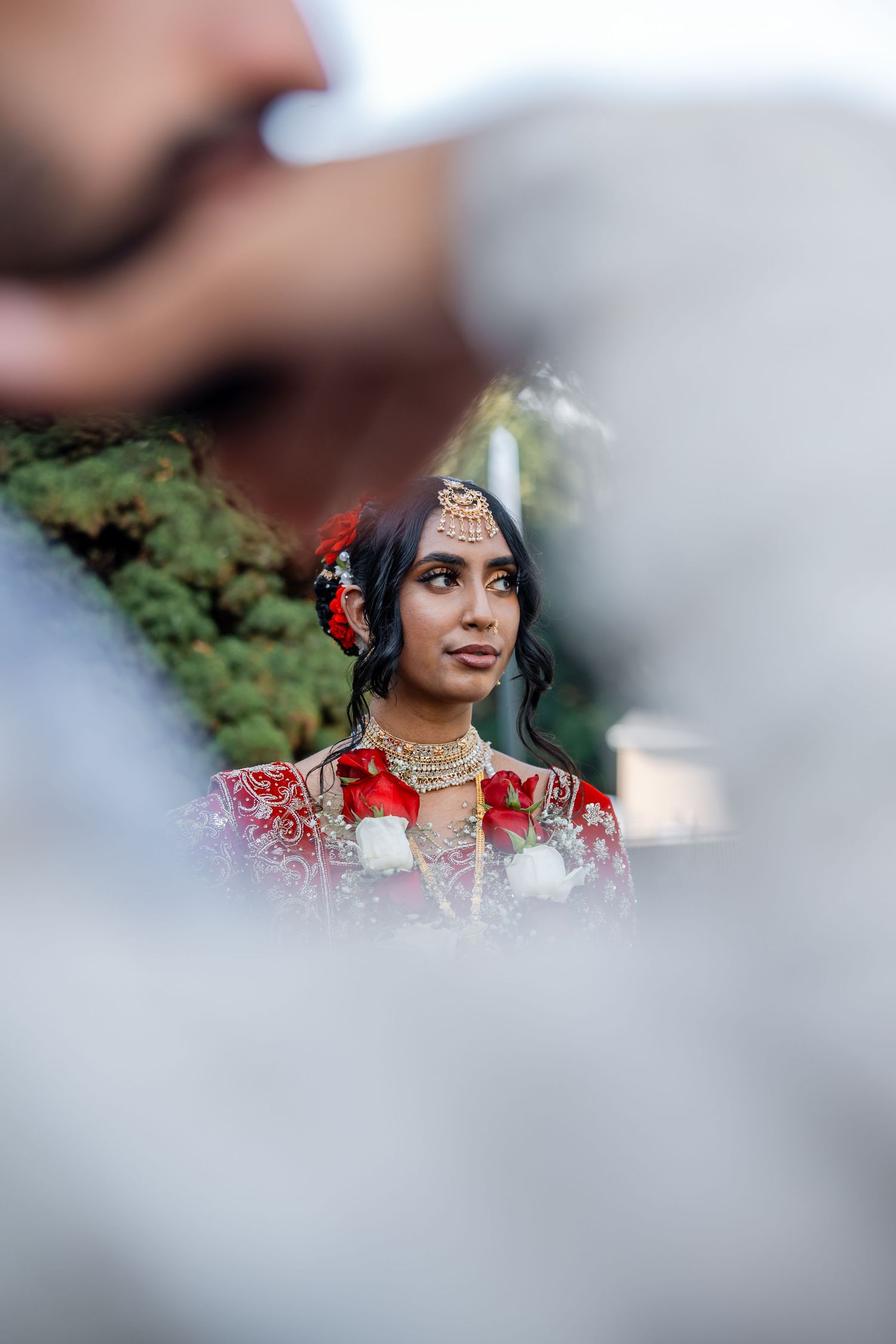 A bride in red and gold traditional attire captured through a creative framed composition.