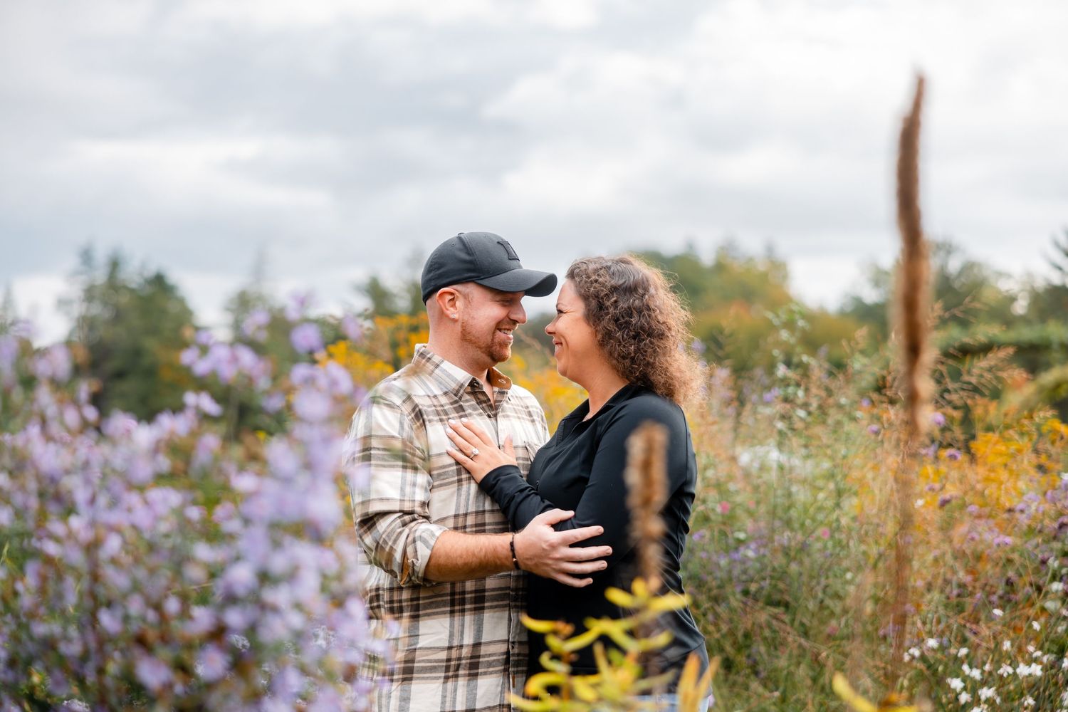 Romantic couple embracing in wildflower meadow with purple and yellow blooms, casual outdoor portrait