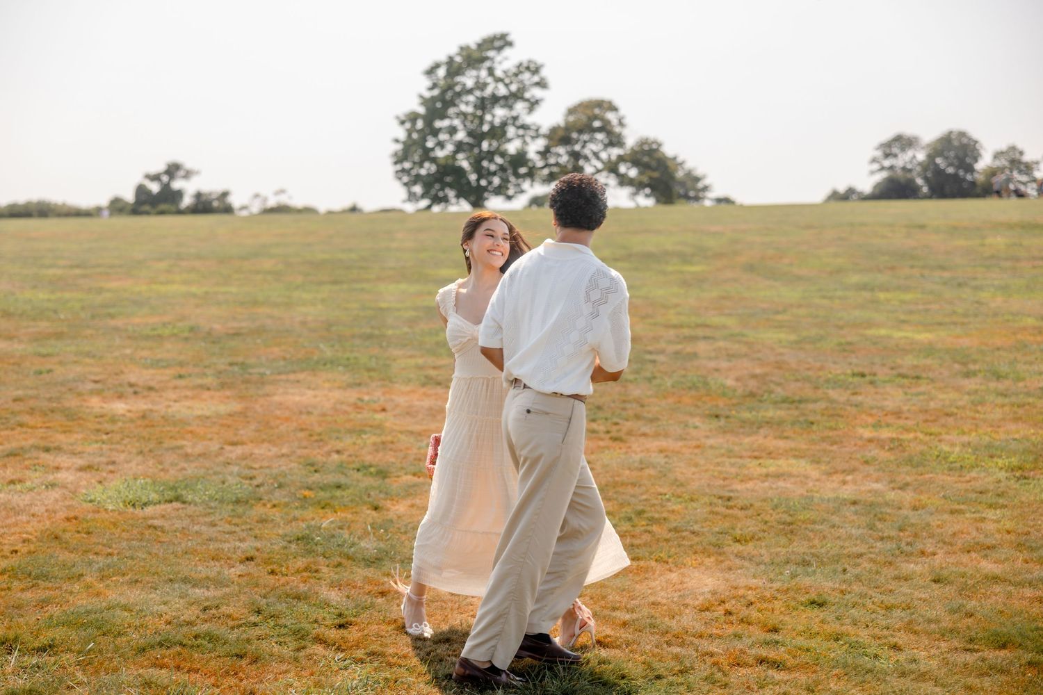 Couple dressed in white walking together across a grassy meadow.