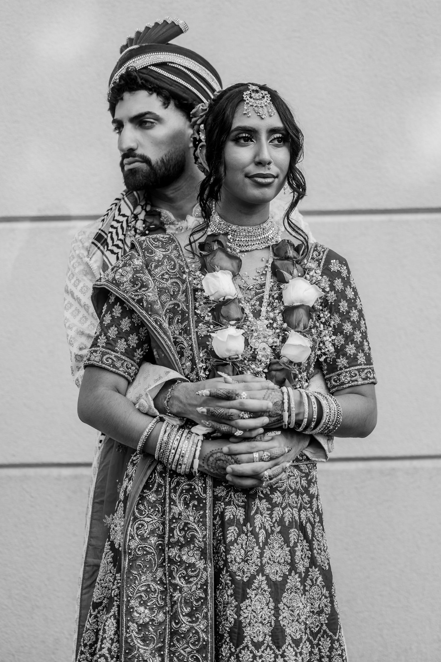 A couple in ornate Indian wedding outfits holding drinks during their celebration.