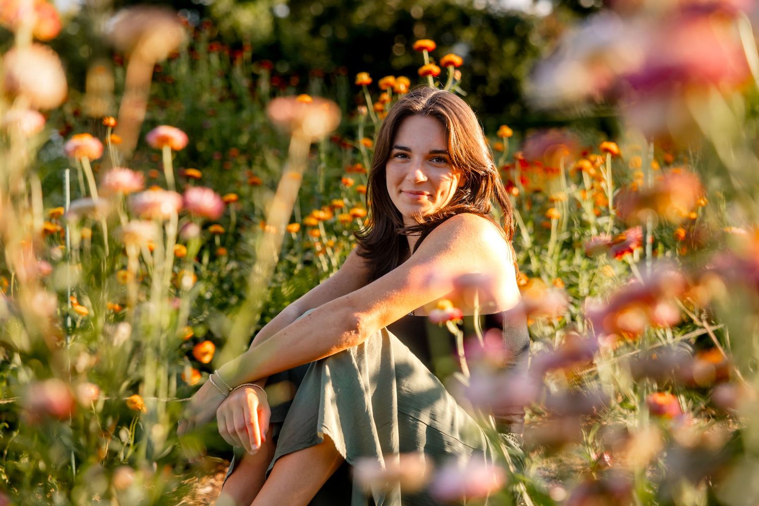 Candid portrait through orange wildflowers in golden summer meadow.